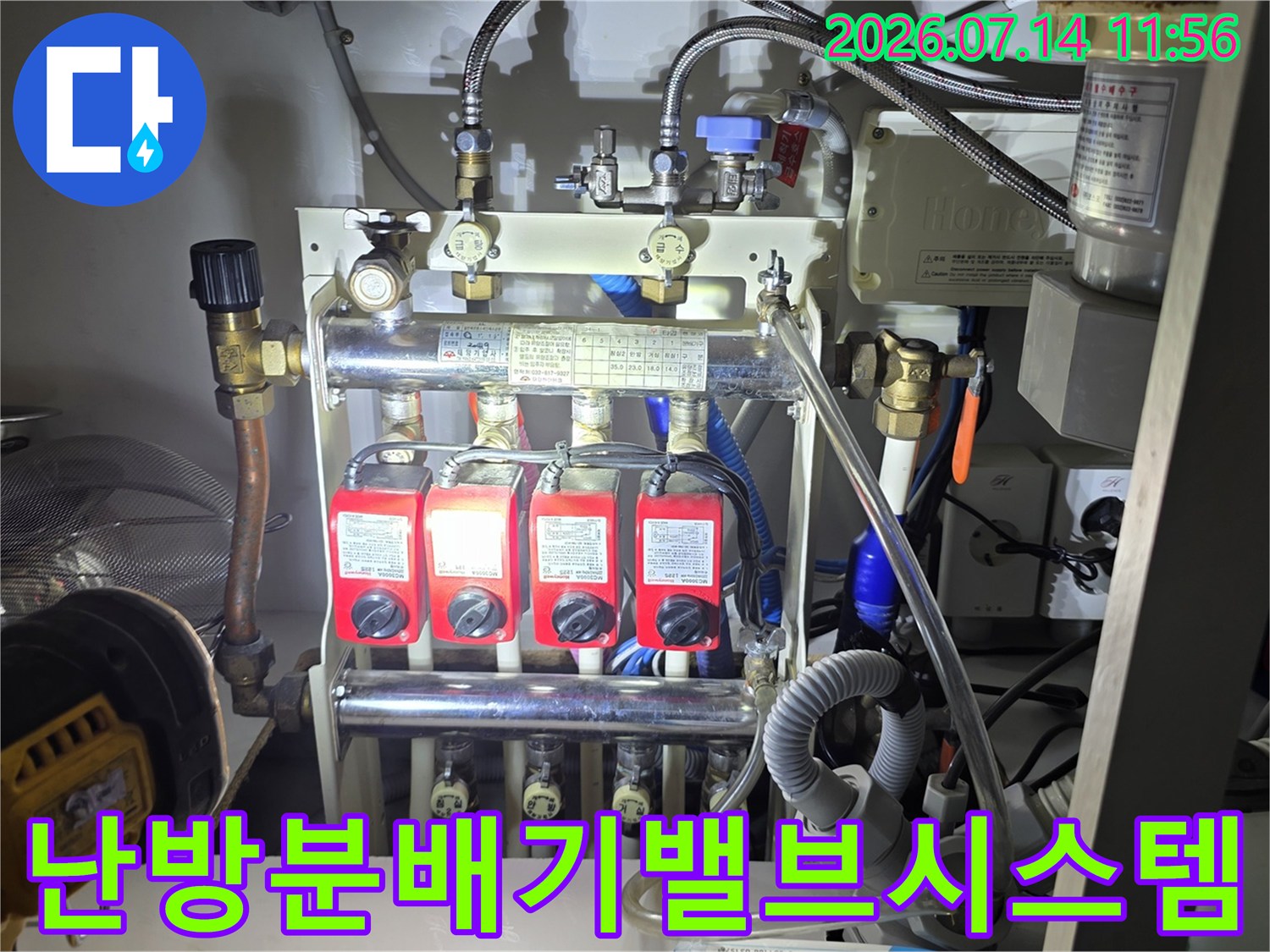 빨간색 밸브 4개가 설치된 금속 재질의 난방 분배기와 복잡한 배관 연결망