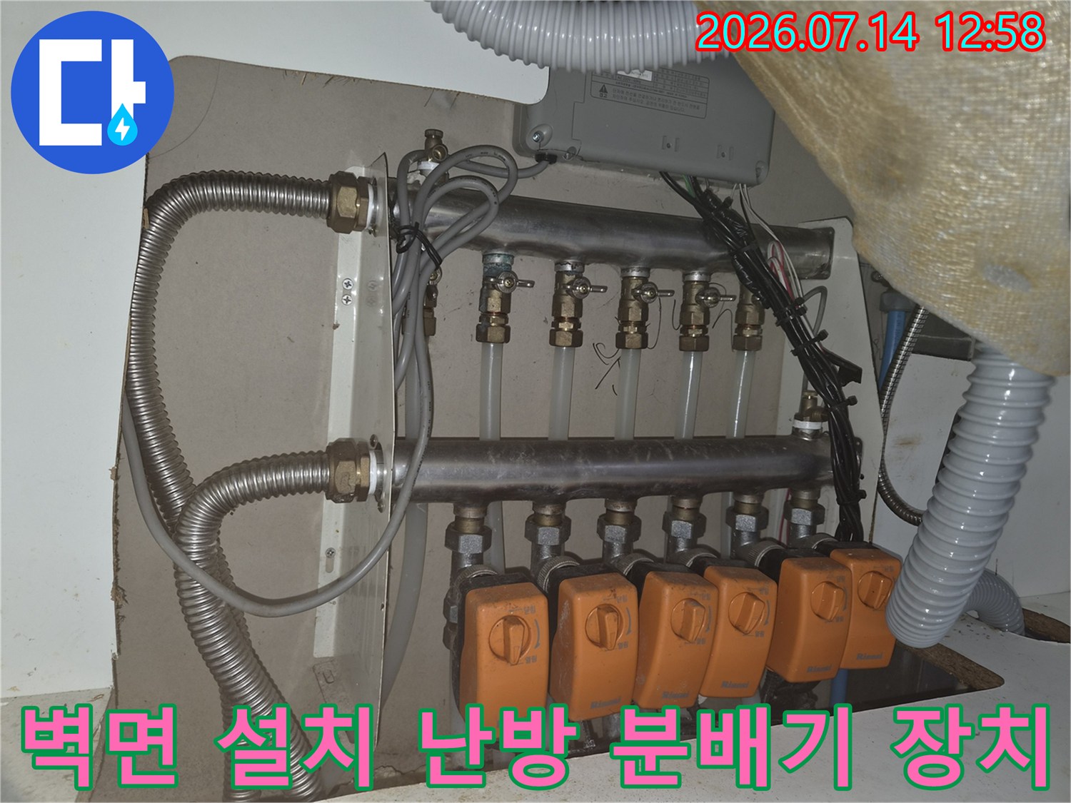 흰색 벽면에-고정되어 있는-금속제 배관과-주황색 밸브들의 배열