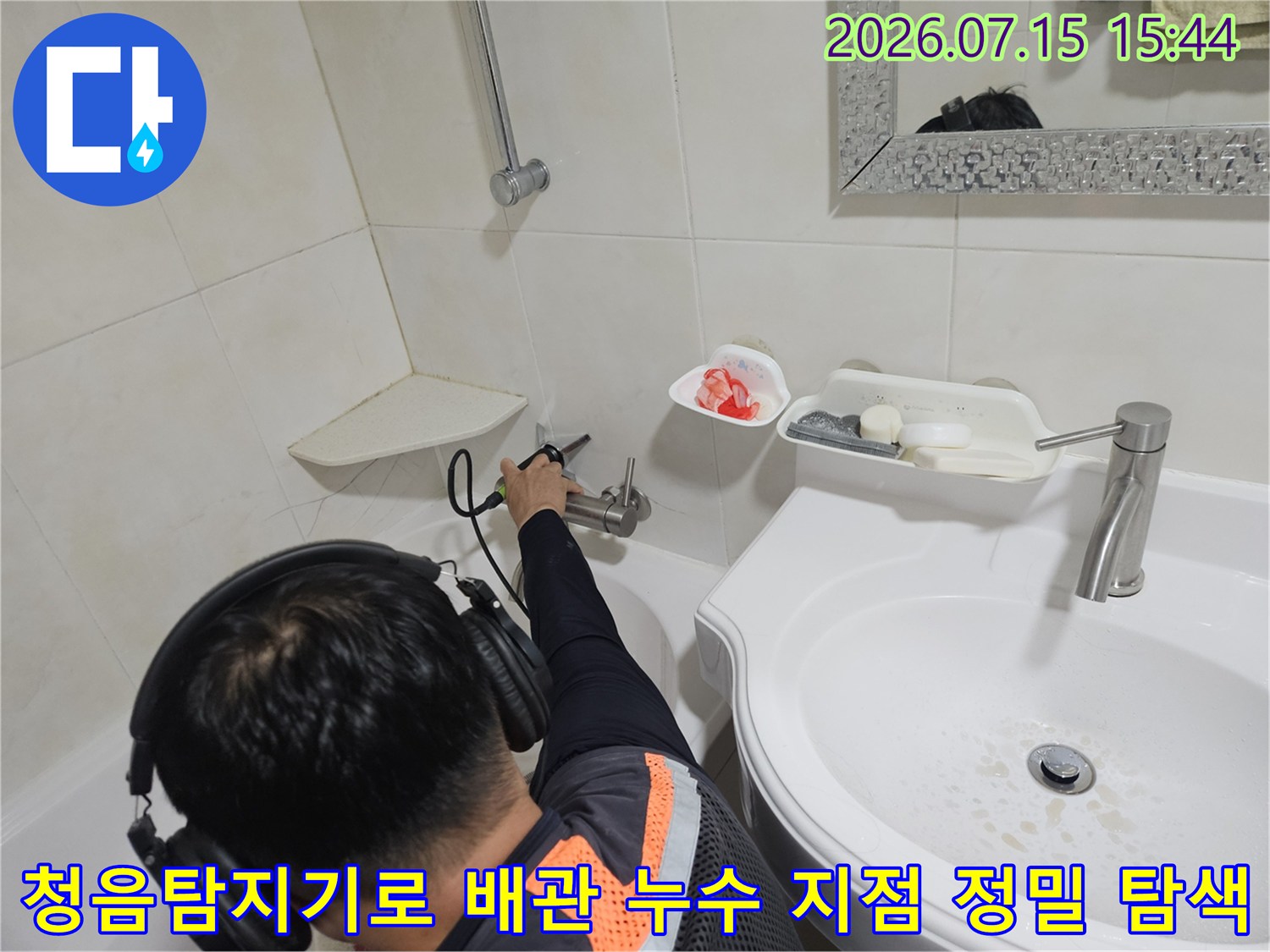 기술자가 청음식 탐지기를 사용하여 세면대 하부 배관의 누수 위치를 파악하는 모습