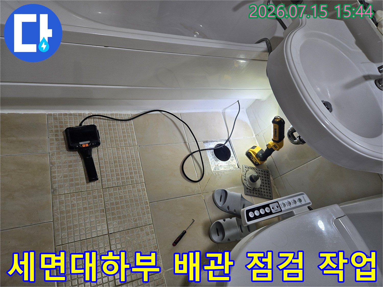 세면대 아래쪽 노출된 배관과 전동 드릴 및 누수 탐지 장비가 있는 모습
