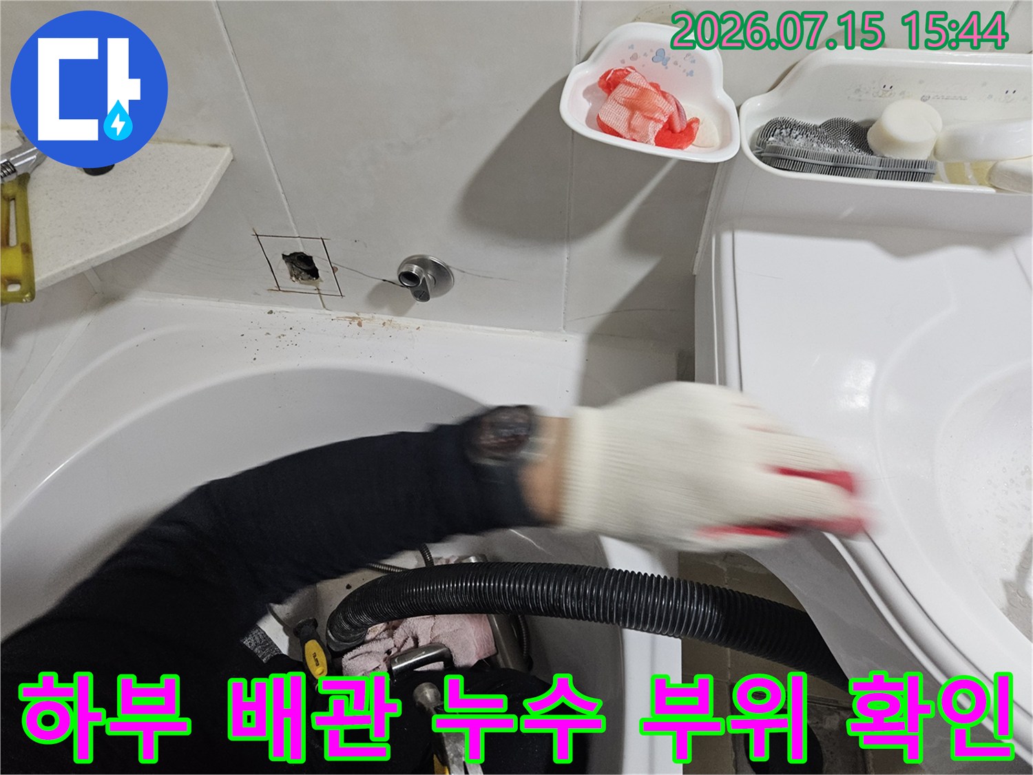 작업자가 세면대 아래쪽의 노후된 배관을 손으로 가리키며 점검하는 사진