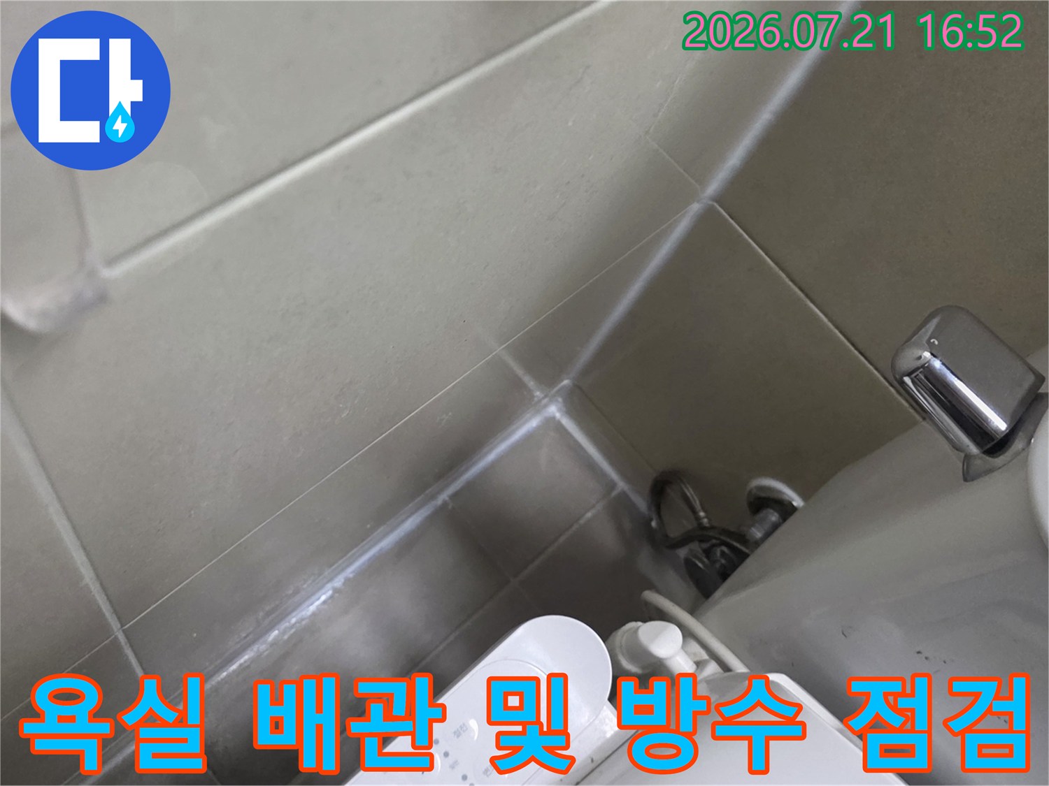 변기 옆 배수구 주변의 노출된 배관과 타일 마감 부위를 점검하는 모습
