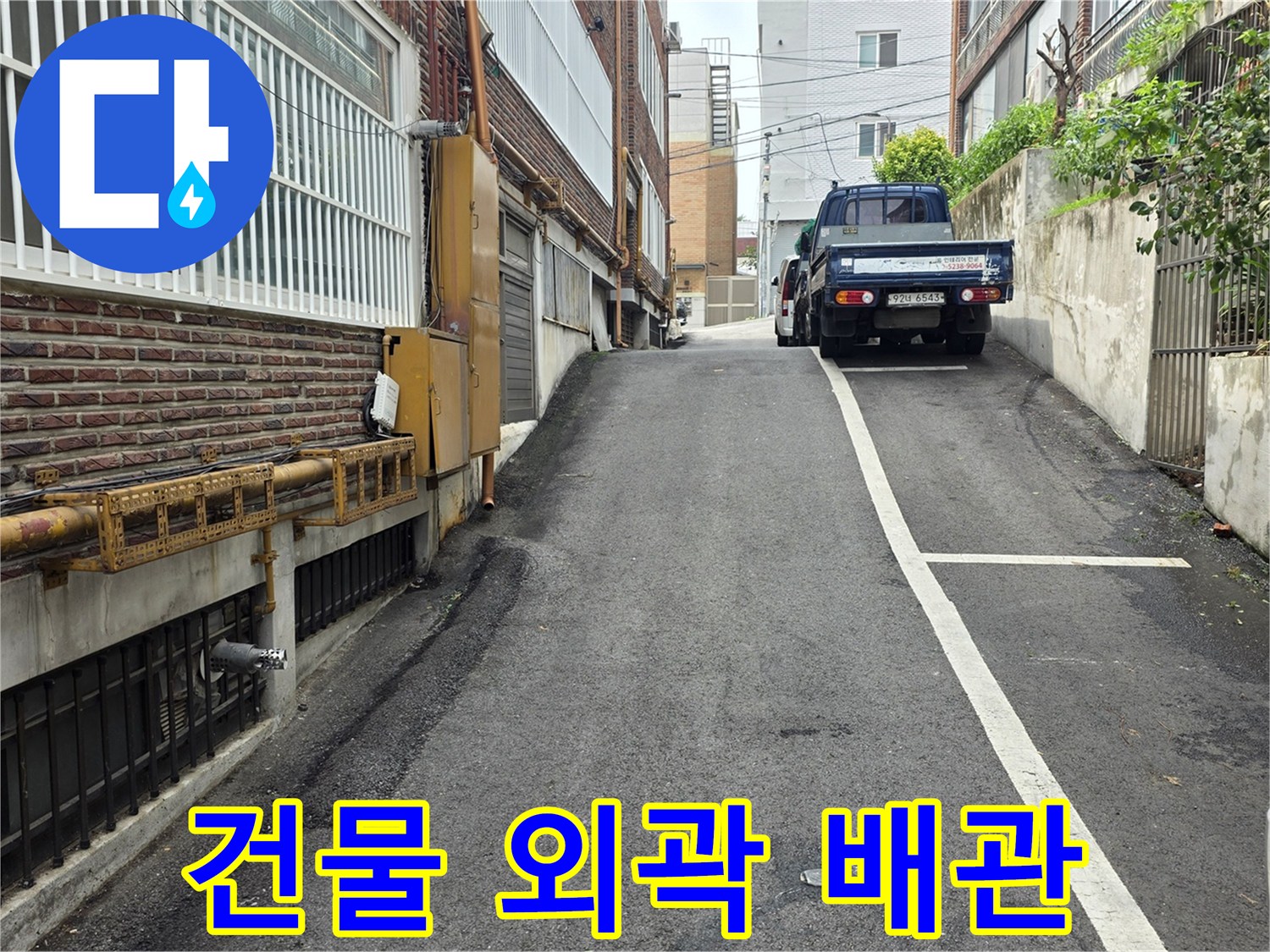 벽면에 고정된 노란색 배관과 건물 옆 골목의 모습입니다.