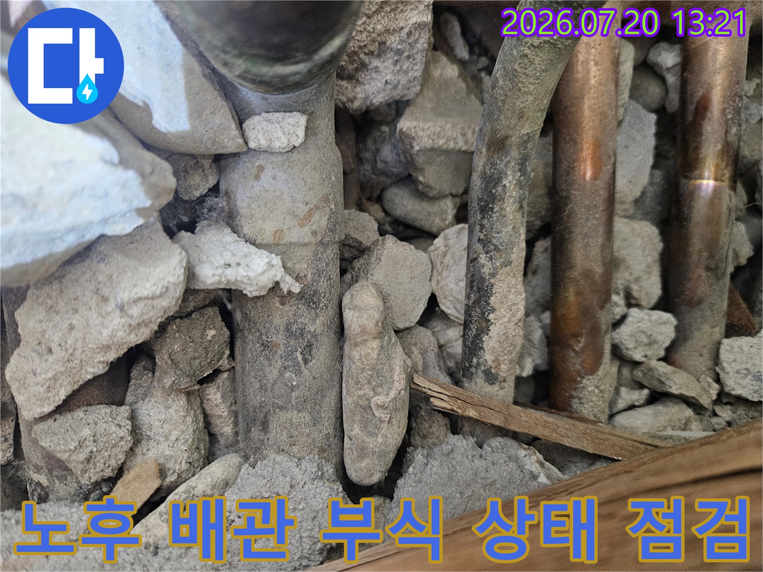부식되고 이물질이 묻은 노출 배관과 주변 석재 파편들