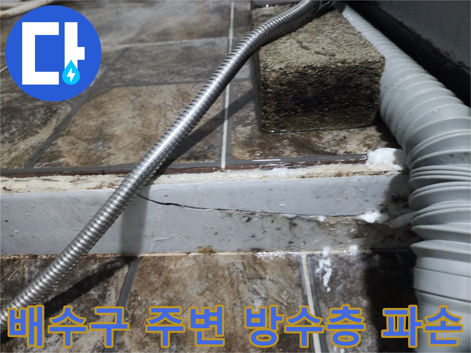 배관 주위의 깨진 마감재와 타일 사이 균열을 근접 촬영한 이미지입니다.