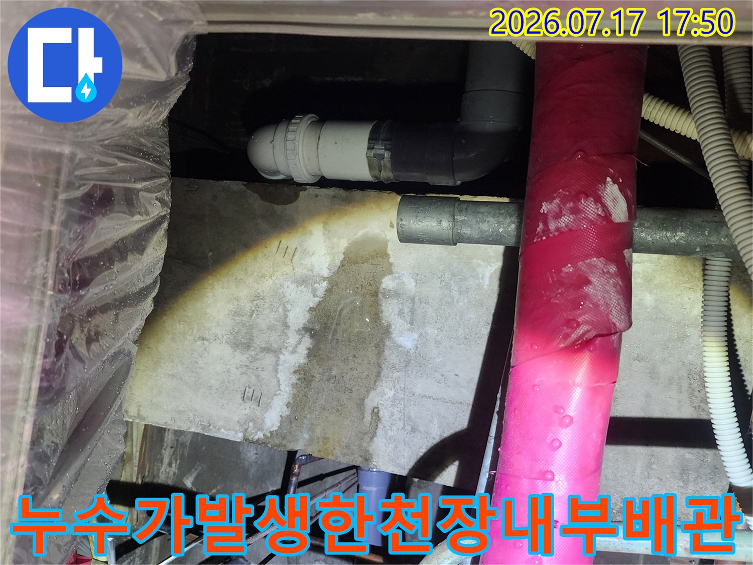 분홍색 보온재가 씌워진 배관 아래로 회색 배수관이 연결되어 있는 천장 내부 사진