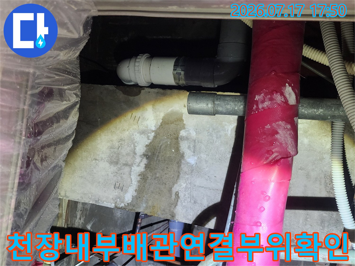 천장 속 분홍색 보온재 배관과 회색 플라스틱 배수관이 교차하는 지점의 모습