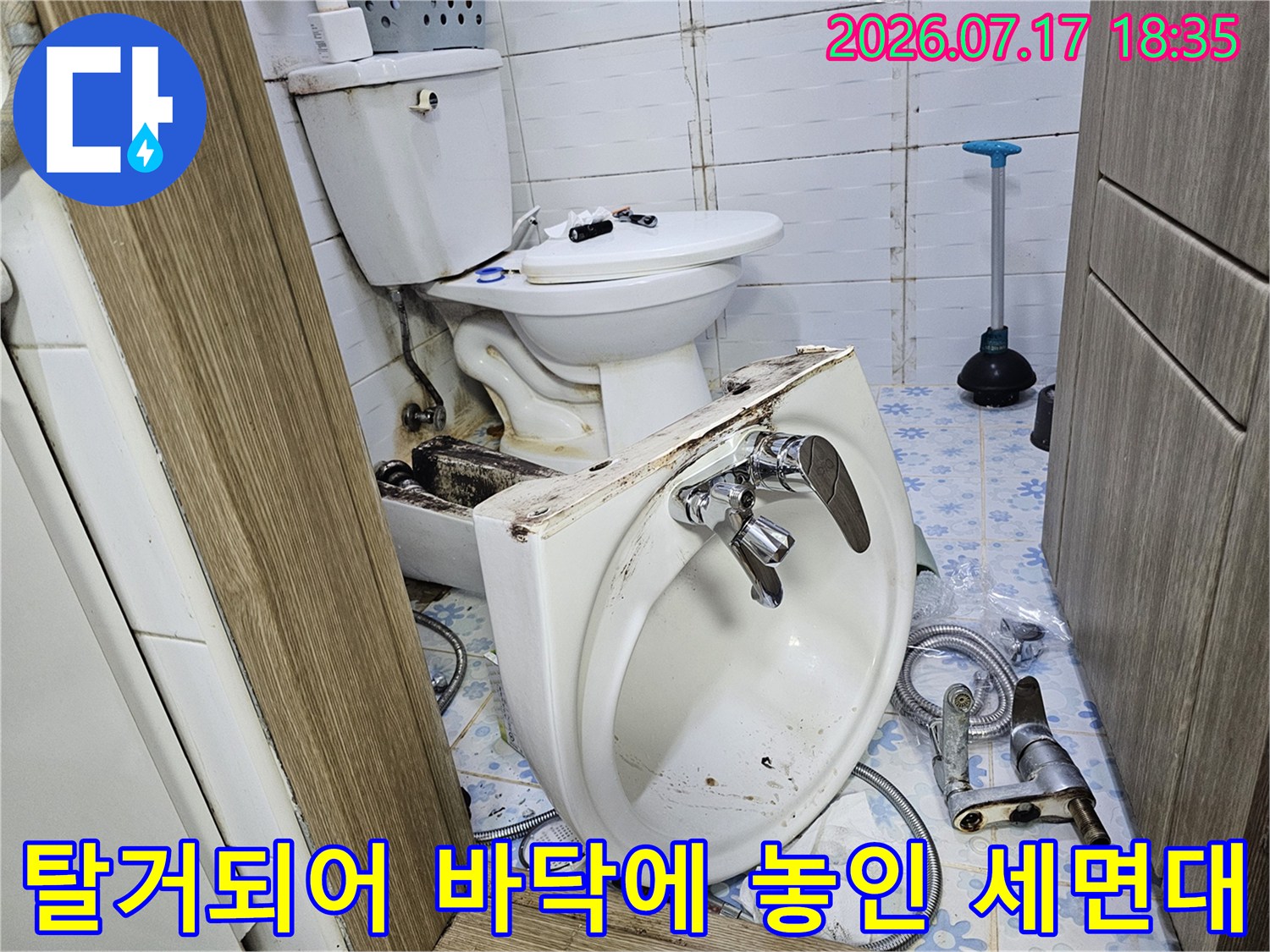 하얀색 도기 세면대가 타일 바닥에 놓여 있고-뒤쪽에 변기가 배치됨