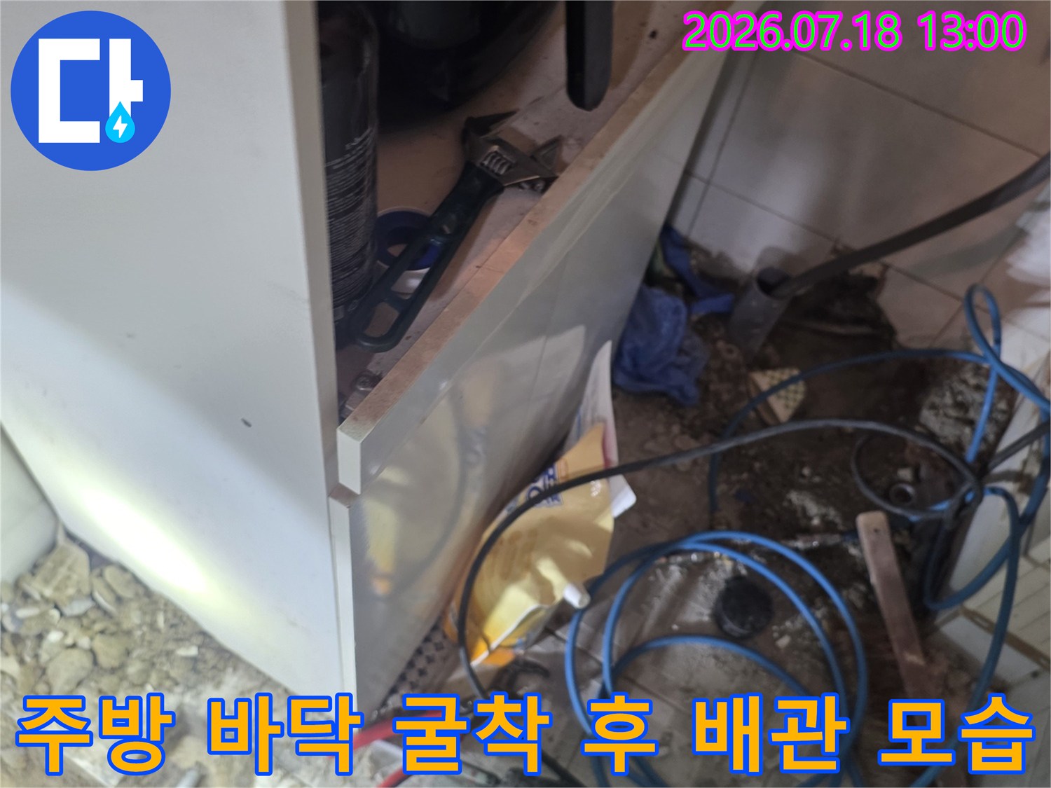 싱크대 아래쪽 바닥 타일을 제거하고 드러난 파란색 플라스틱 수도 배관과 작업 공구들