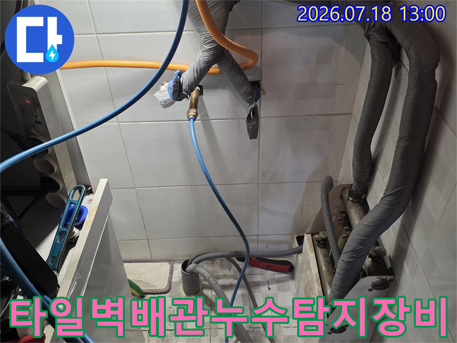 하얀 타일 배경의 벽면에 회색 배관과 파란색 탐지 호스가 연결된 모습의 사진