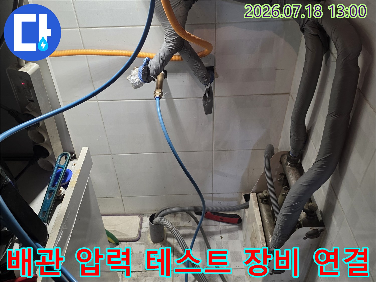 흰색 타일 벽면의 회색 보온재 배관들과 그 아래 연결된 파란색 탐지 호스-누수 진단 현장