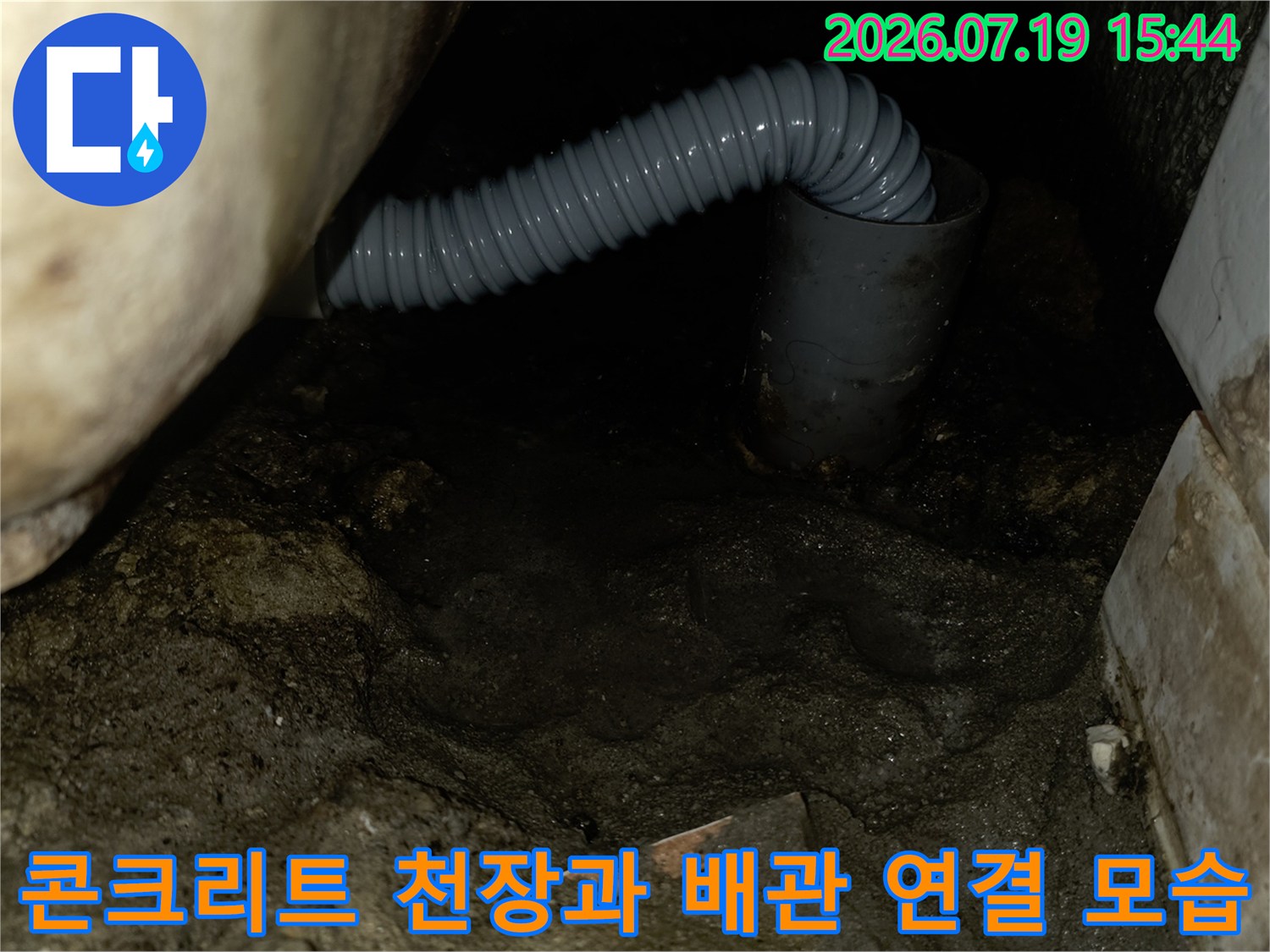거친 콘크리트 면 아래로 설치된 회색 하수 배관의 굴곡진 모습