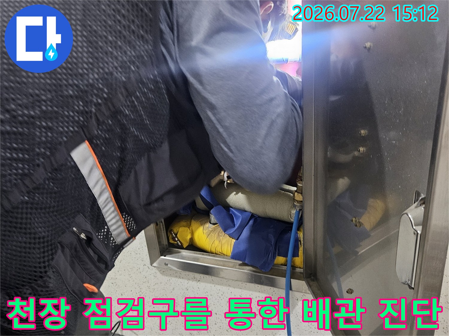 엔지니어가 화장실 천장 점검구 내부로 상체를 넣어 파란색 호스와 노란색 보온재가 감싸진 배관을 세밀하게 살피는 모습