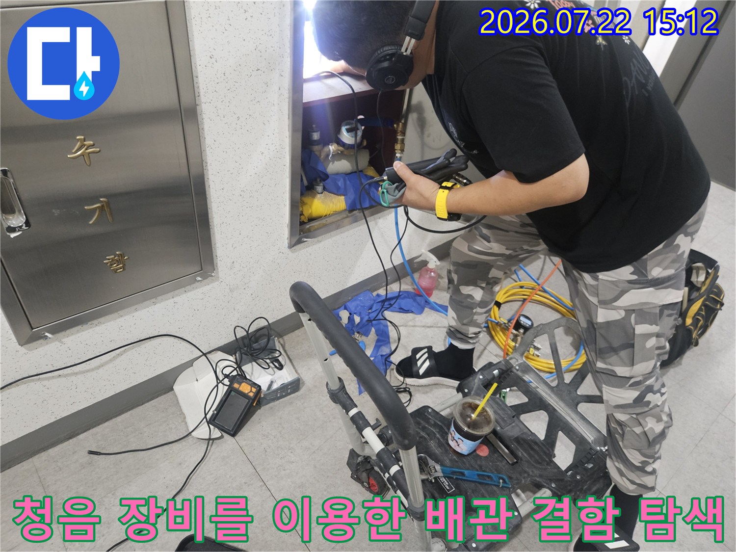 작업자가 벽면의 점검구를 통해 내부 배관에 청음기를 대고 누수음을 체크하는 모습