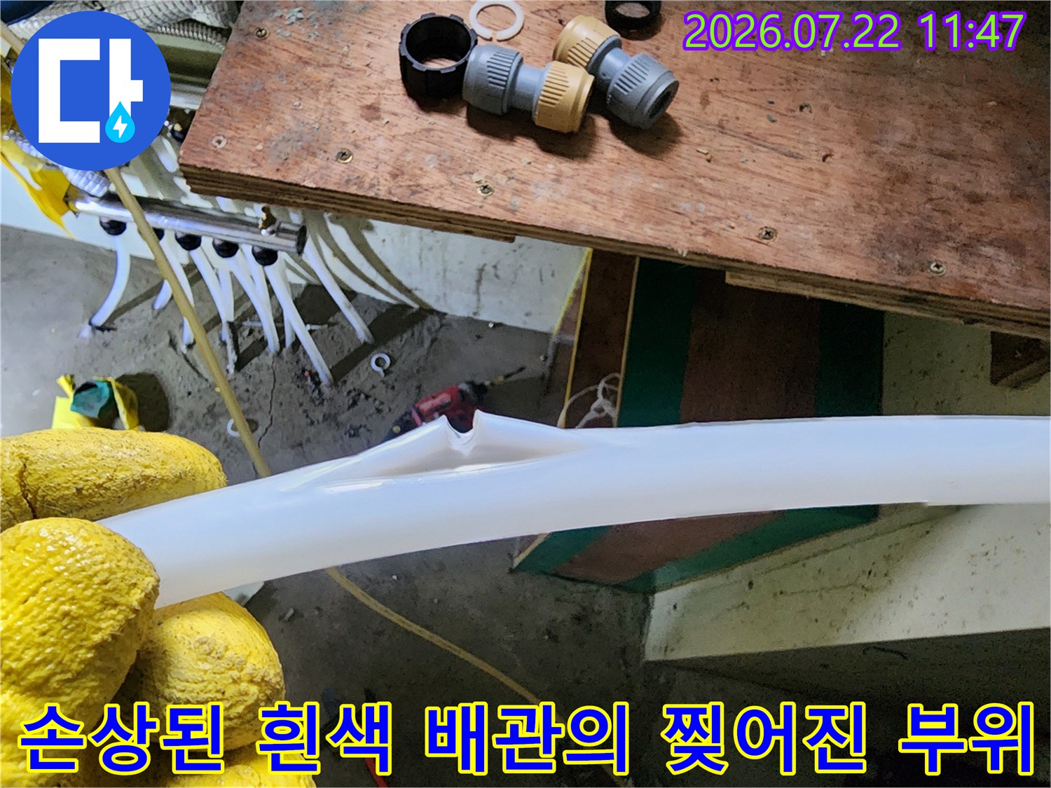 노란 장갑을 낀 작업자가 누수가 발생한 찢어진 형태의 흰색 PEX 배관을 들어 올린 모습