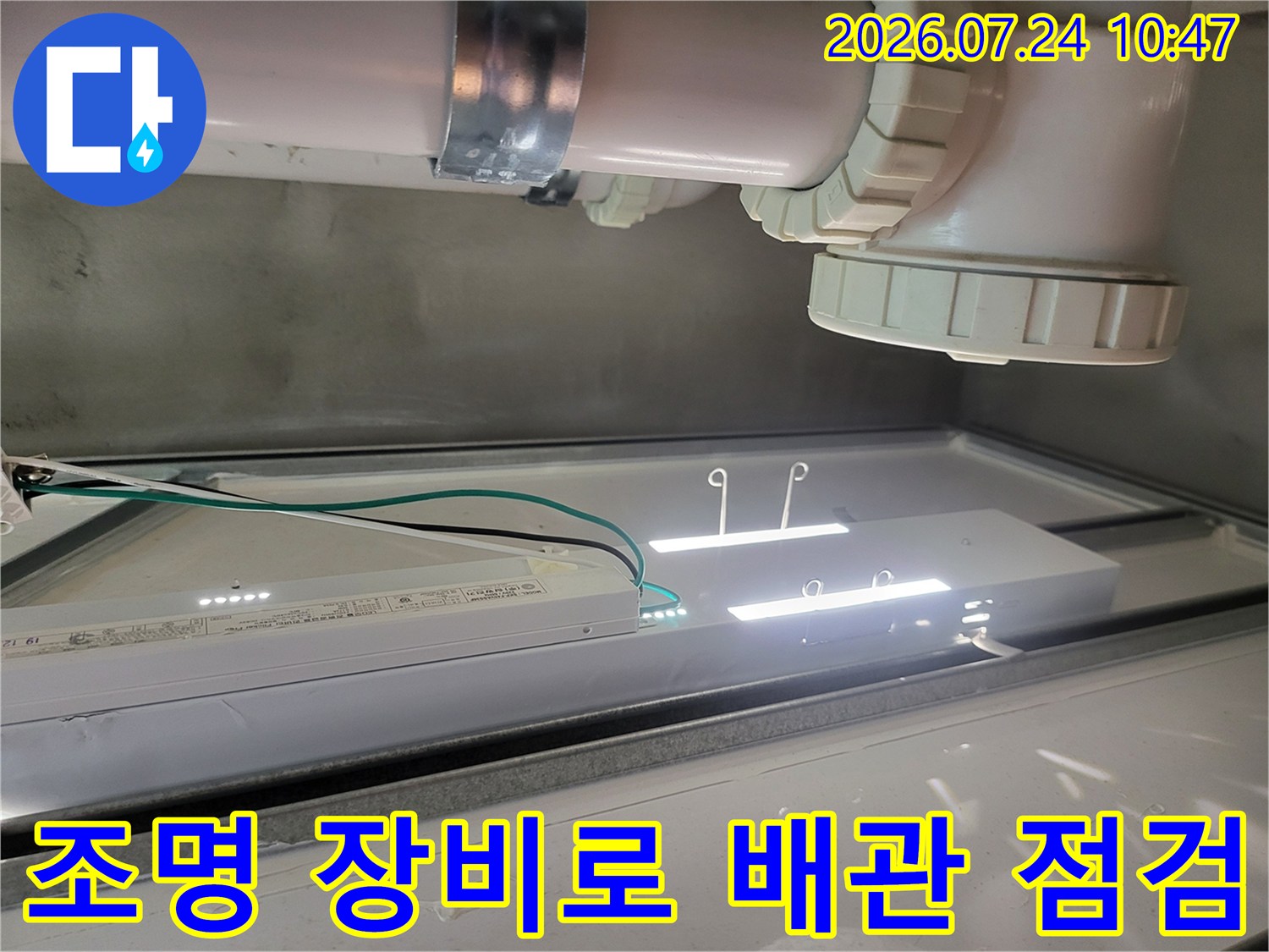 고휘도 조명을 사용하여 싱크대 하부의 복잡한 배수관 연결부를 확인하는 장면