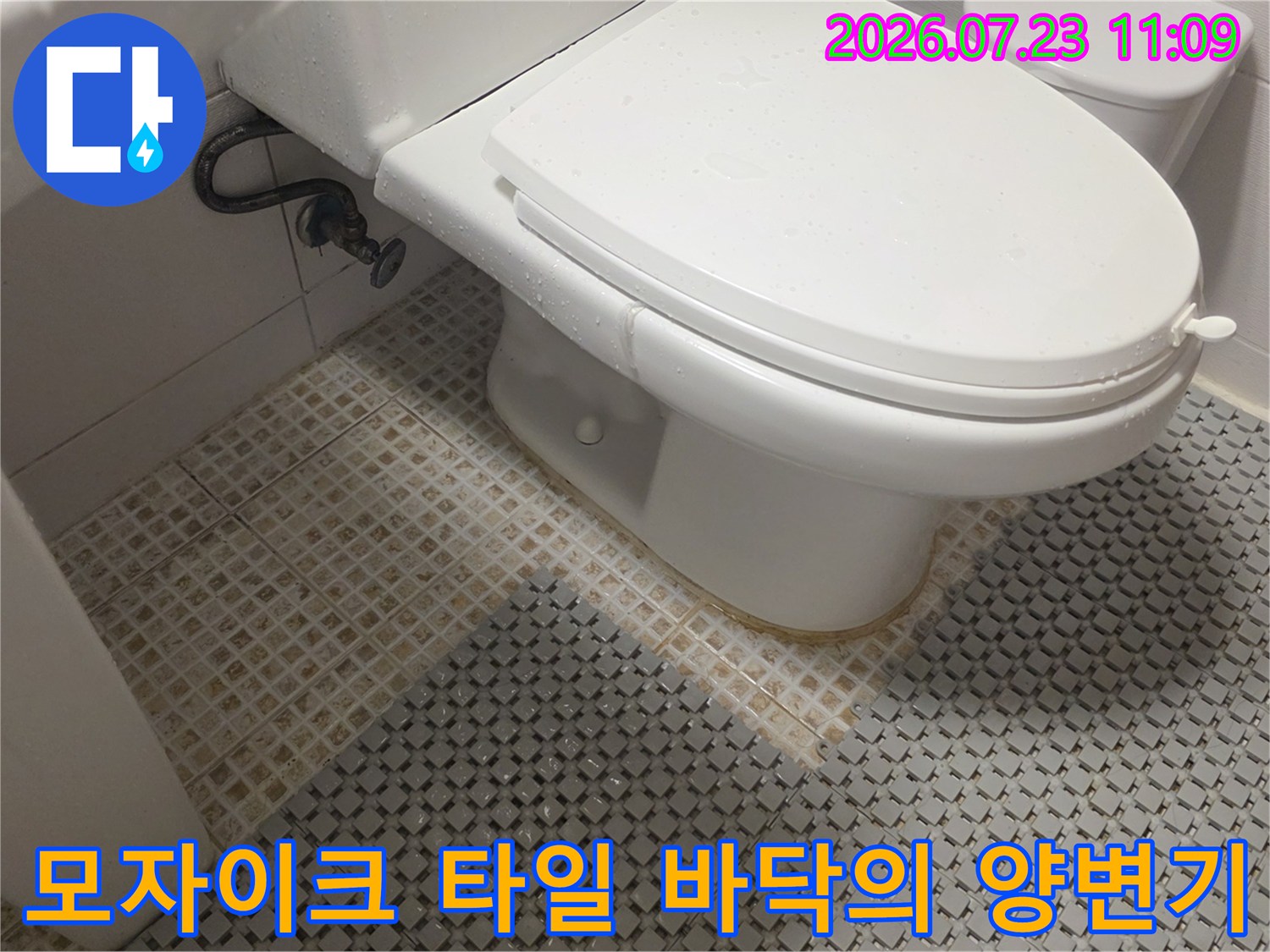 흰색 양변기가 설치된 화장실 내부 모습과 벽면에서 내려오는 금속제 급수 배관