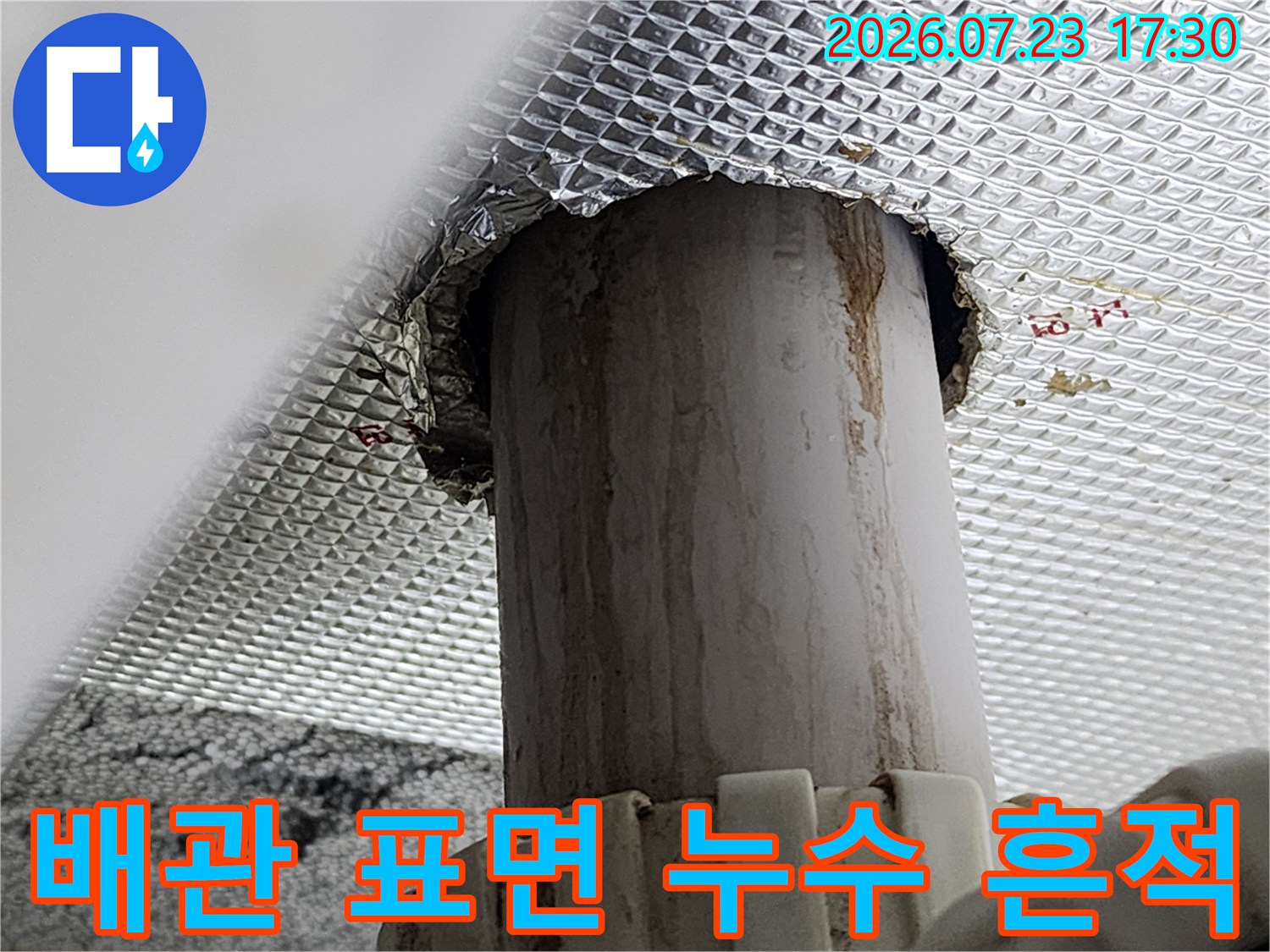 회색 배관 외벽에 세로로 형성된 갈색 누수 얼룩과 은박 마감재-사진