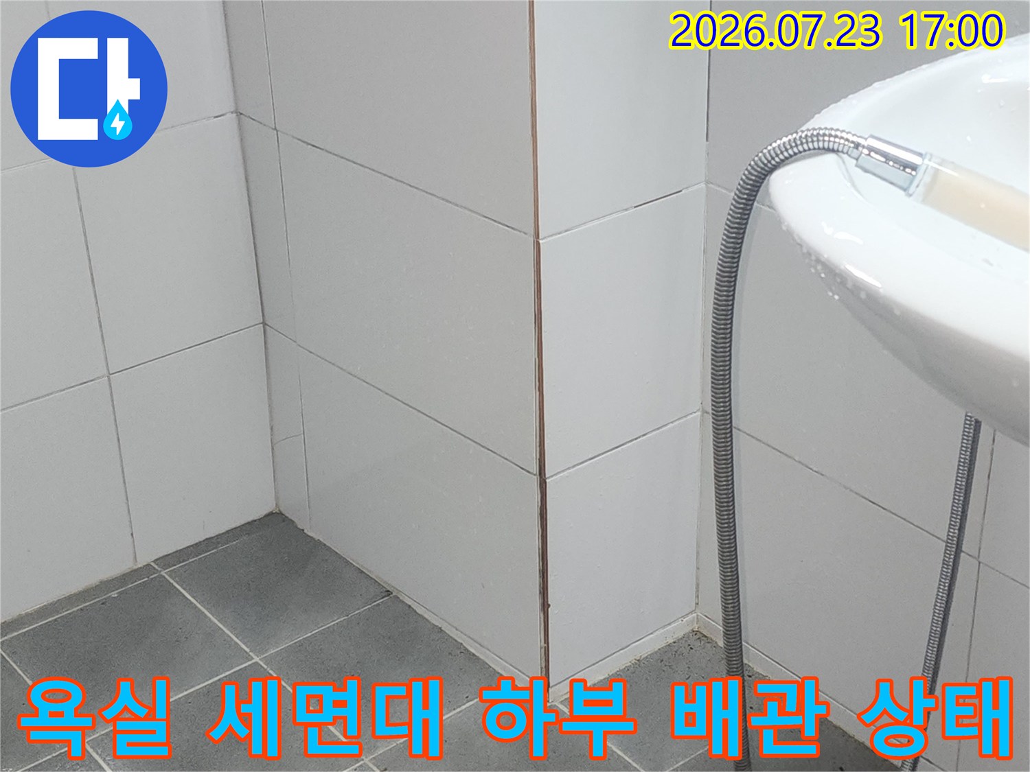 흰색 타일 벽면에 설치된 세면대와 연결된 금속제 샤워 호스가 늘어져 있는 모습