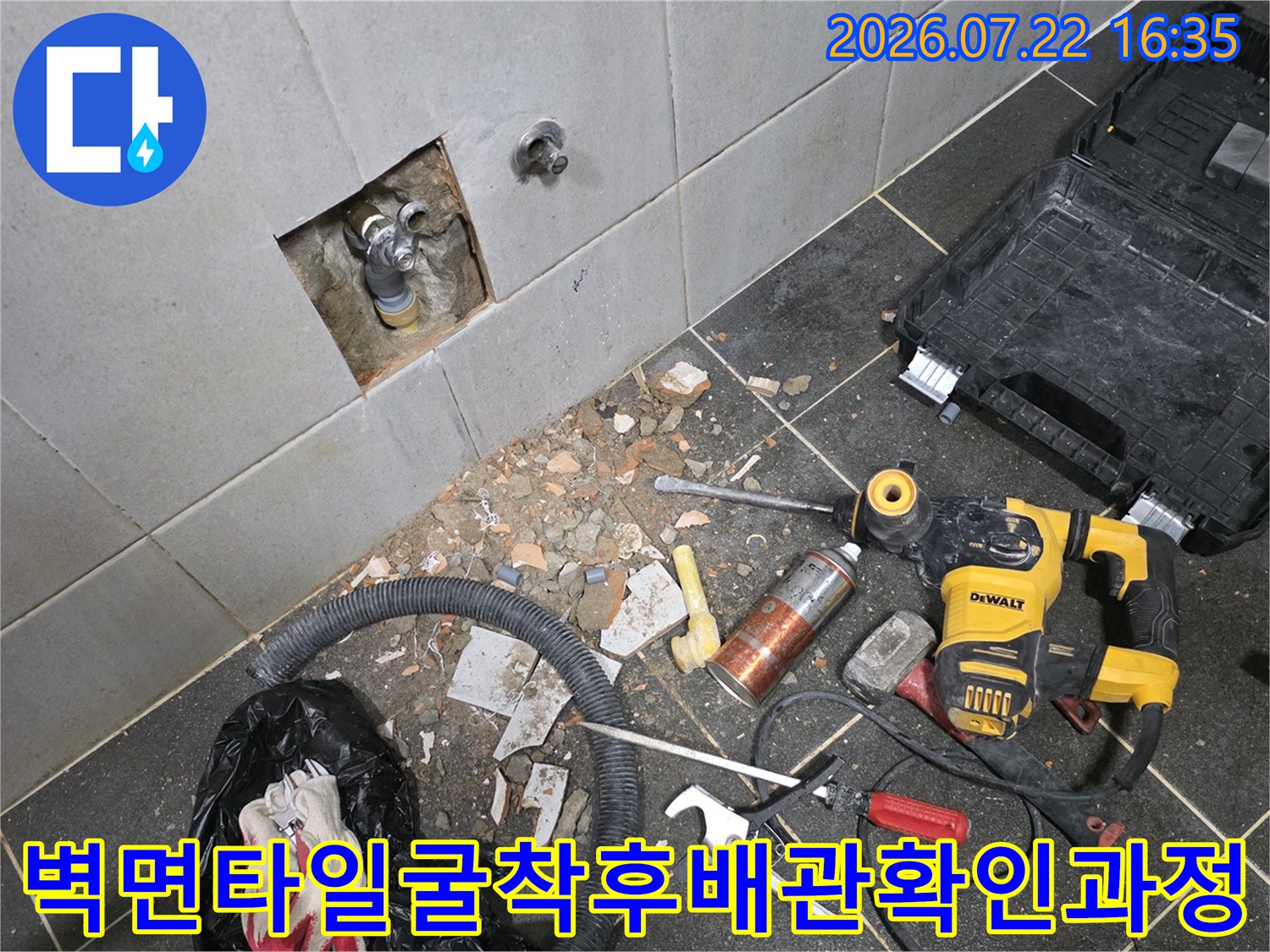 타일을 뚫어 내부 수도 배관을 노출시킨 상태에서 바닥에 전동드릴과 공구들이 배치된 사진