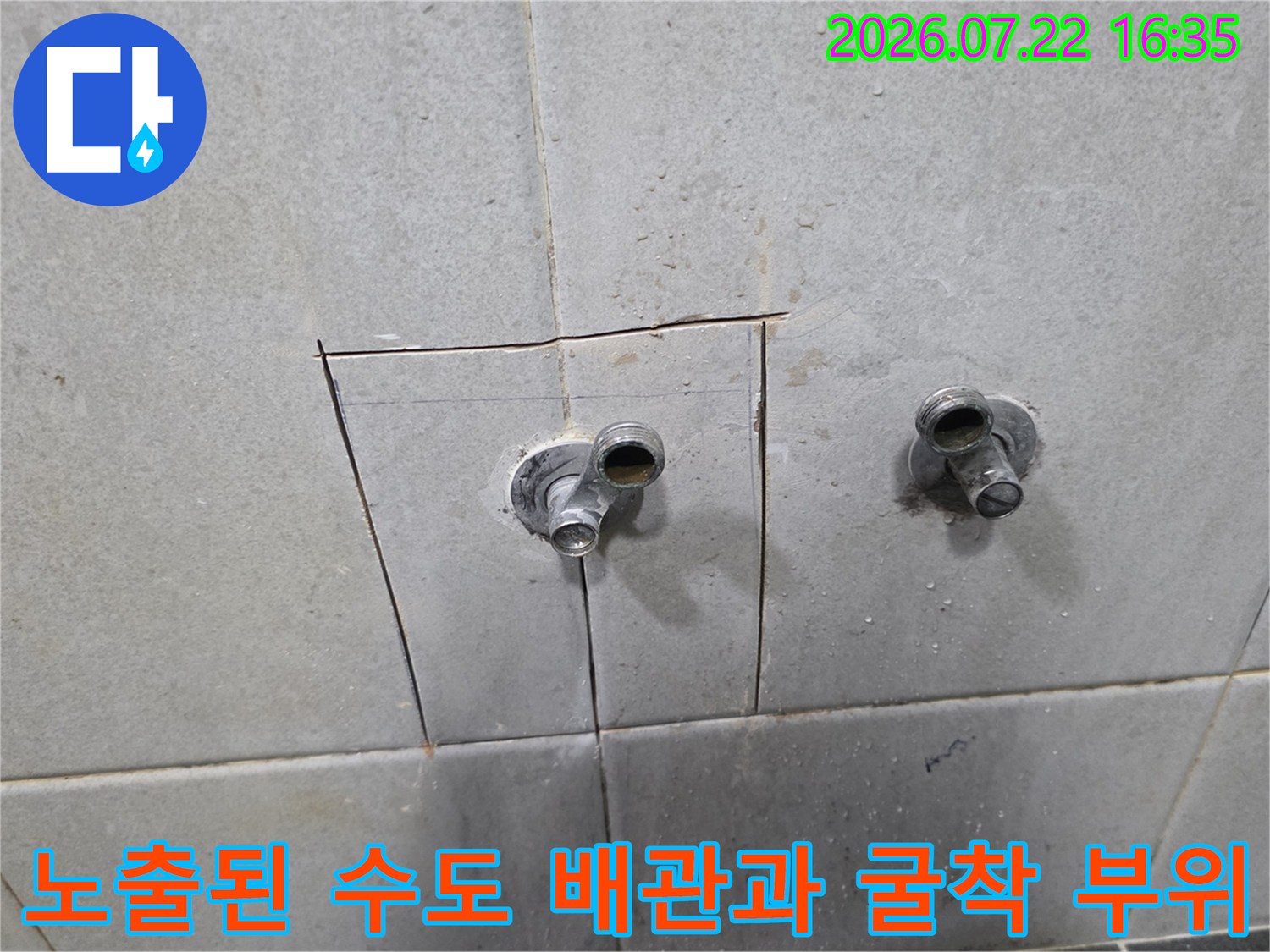 회색 타일 벽면에 사각형으로 파여진 공간 속에 두 개의 수도 배관이 연결되어 있는 모습