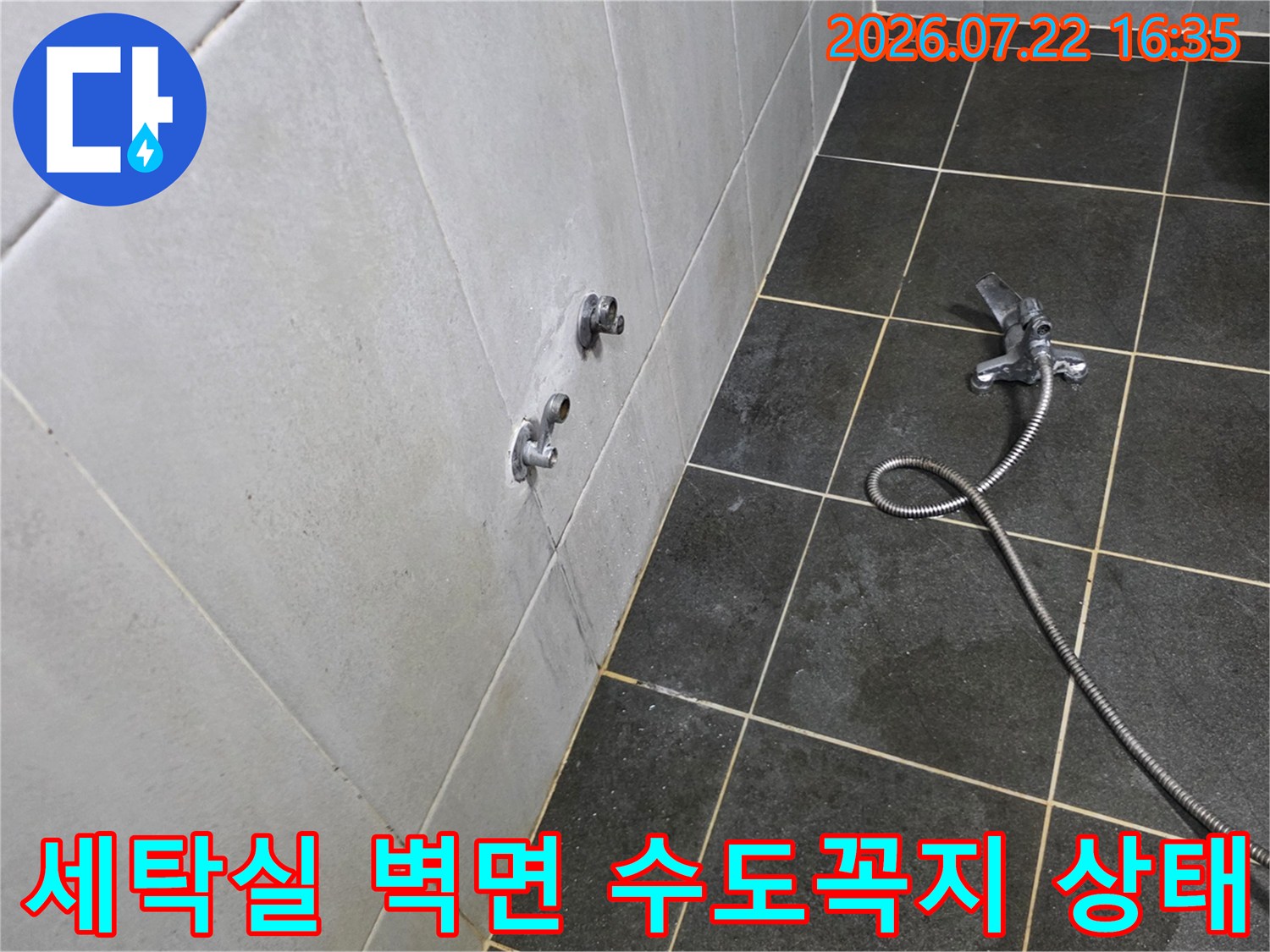 회색 타일 벽면에 설치된 두 개의 수도꼭지와 바닥에 놓인 샤워 호스-누수 점검 전 모습