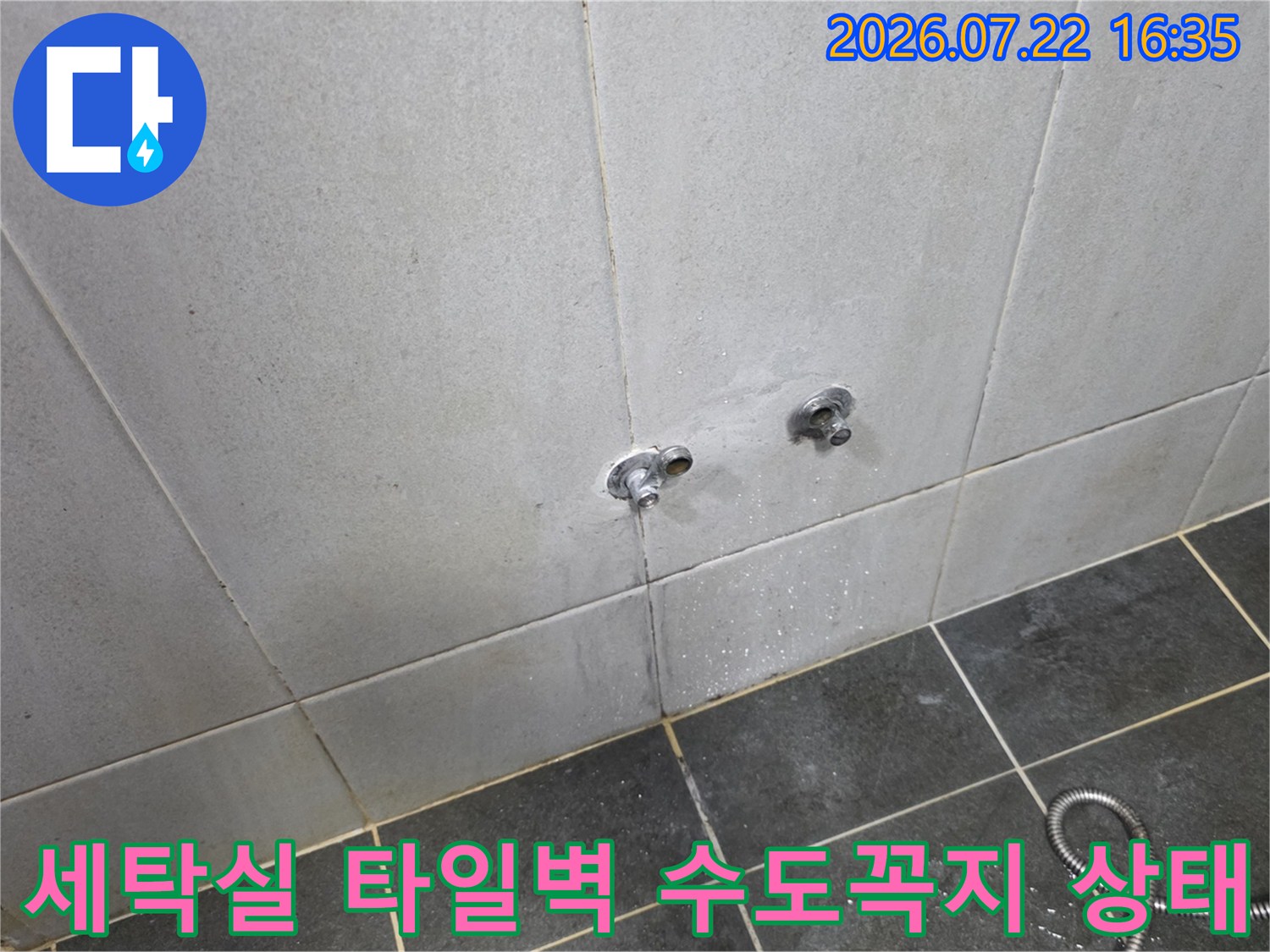 회색 타일 벽면에 설치된 두 개의 수도꼭지와 바닥의 샤워 호스-누수 점검 전 모습