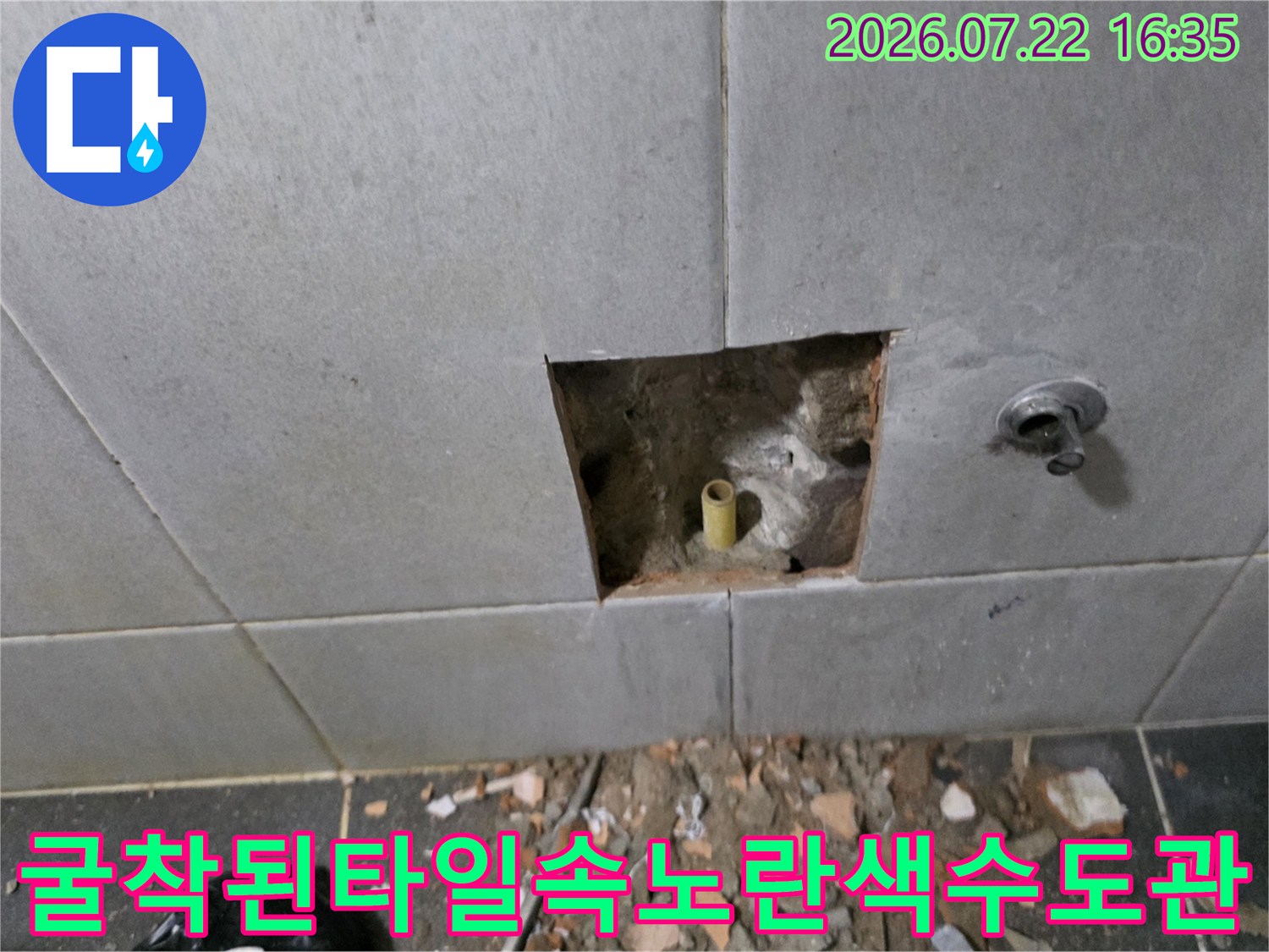 회색빛의 타일 벽면 일부가 제거되어 내부 노란색 배관이 외부로 노출된 사진