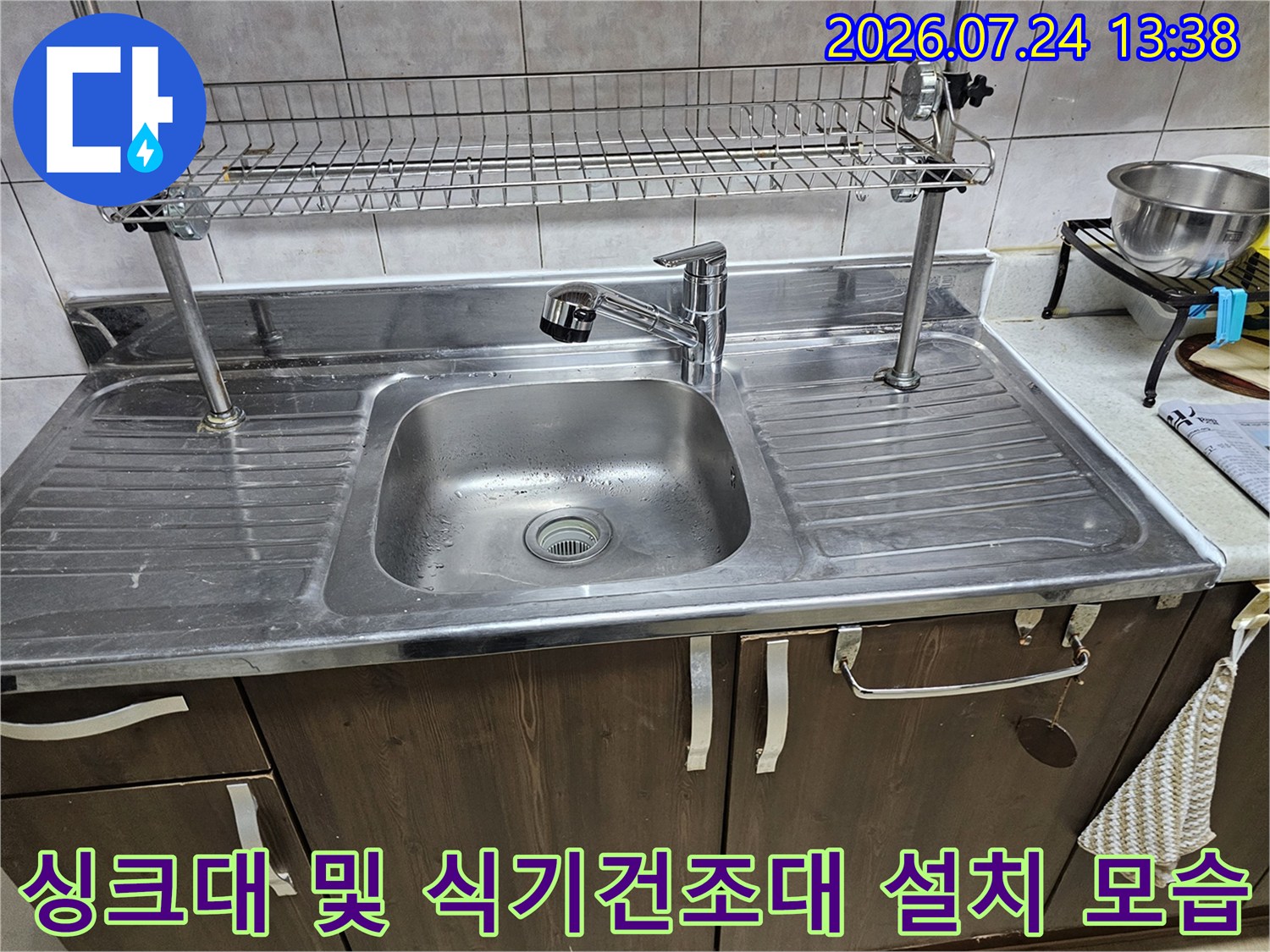 금속제 싱크대 볼과 수도꼭지 그리고 상부의 와이어 선반이 보이는 주방 모습
