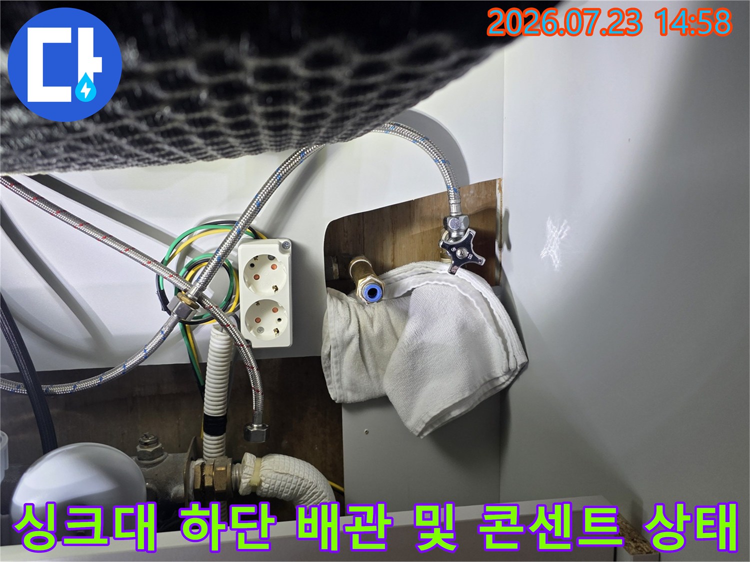 싱크대 아래-급수 호스와 전원 콘센트-그리고 흰색 천이 덮인 배관 연결 부위