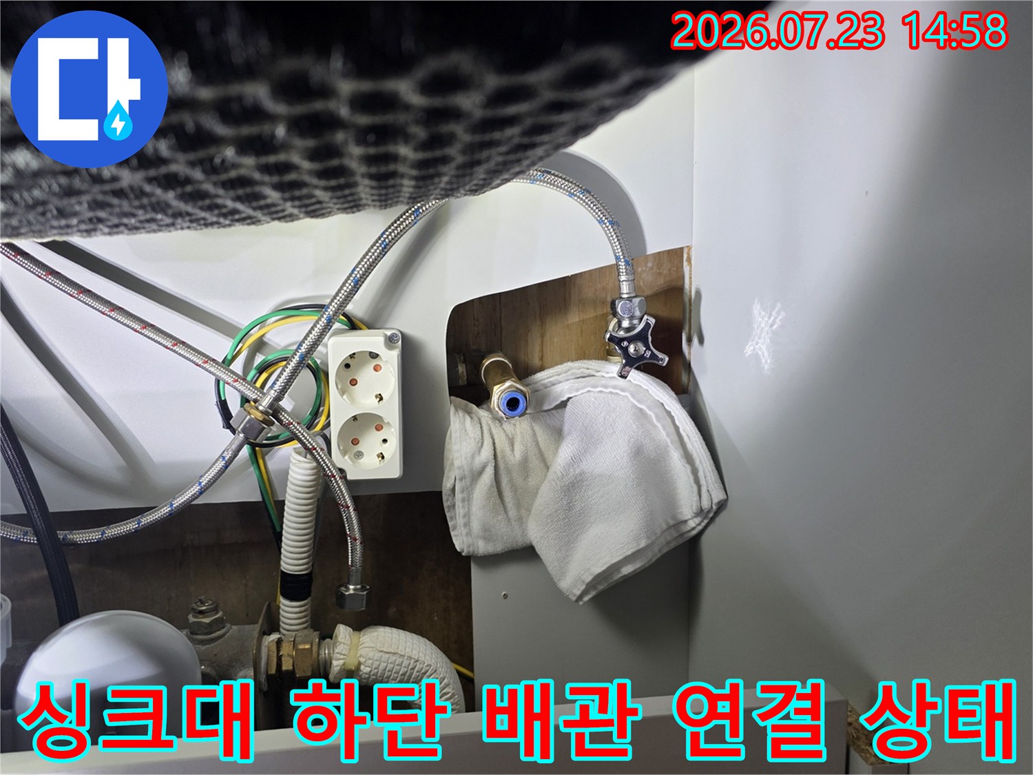 주방 싱크대 아래-금속제 급수 배관과 전원 콘센트가 설치된 모습