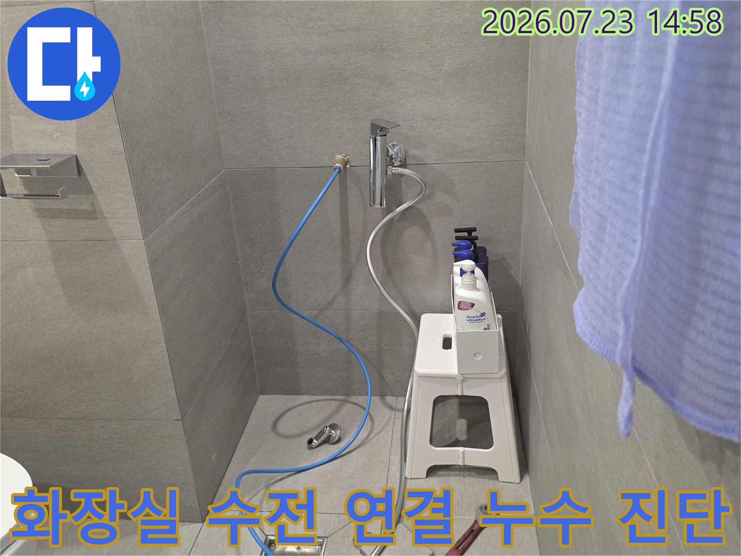 회색 타일 벽면의 수도꼭지에 파란 호스가 연결되어 있는 누수 검사 현장