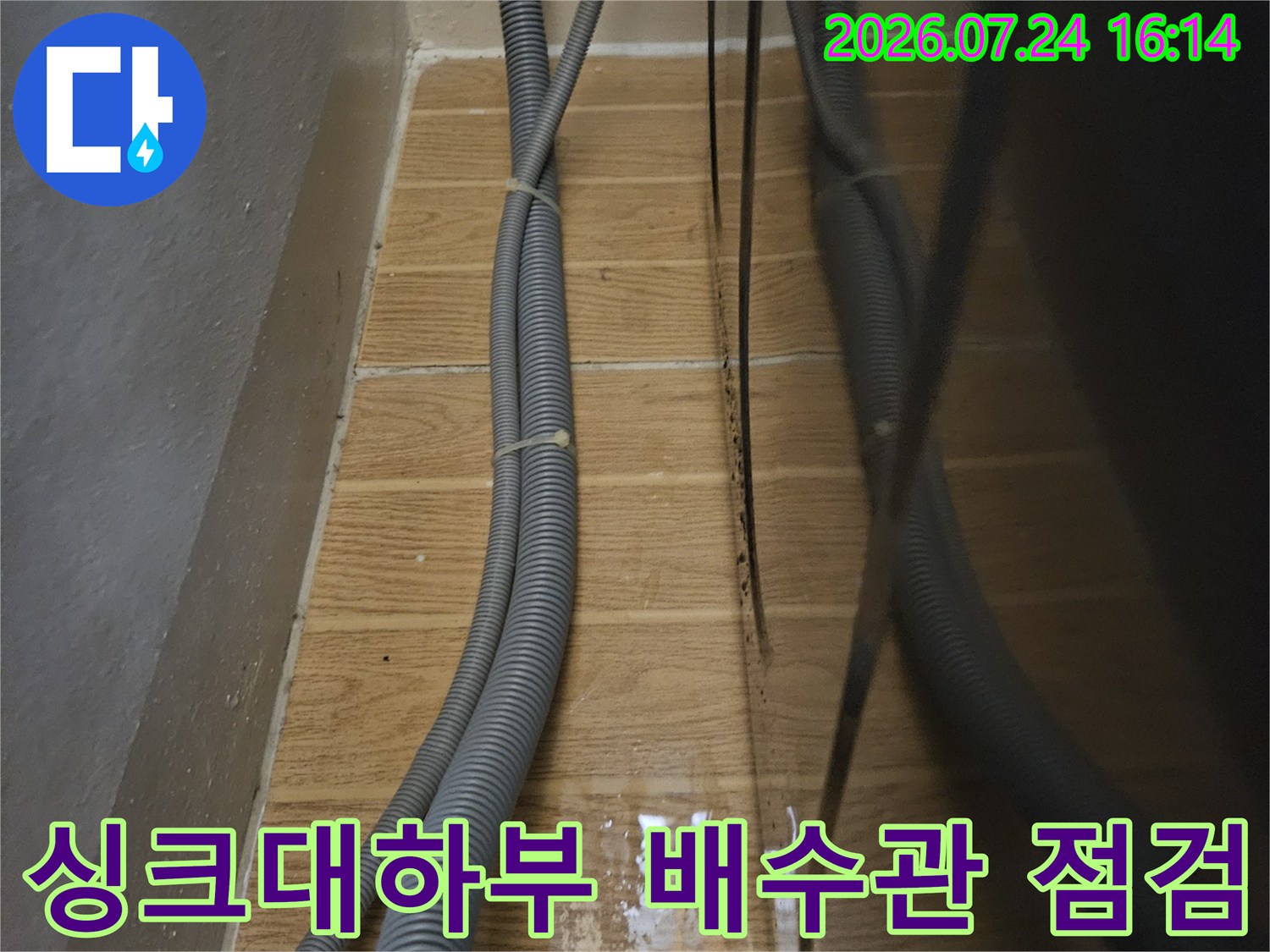 싱크대 하부장 내부의 회색 배수 호스와 벽면 연결 부위 점검 모습