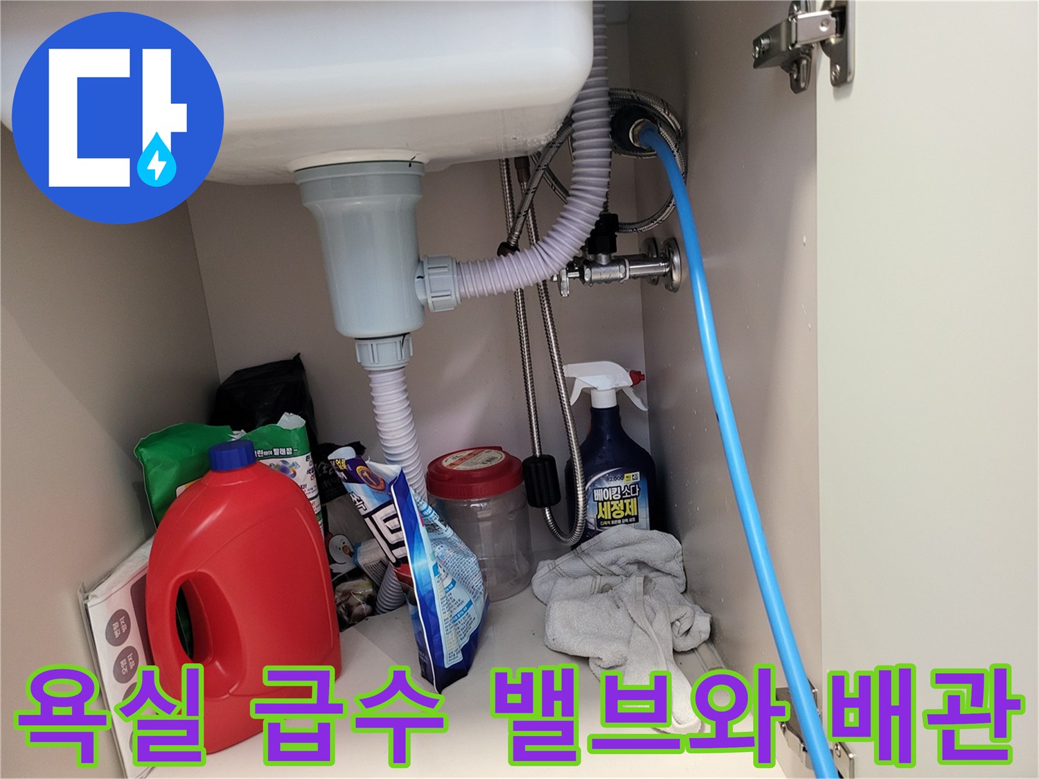 세면대 아래쪽 벽면에 설치된 급수 밸브와 은색 금속 배관의 모습입니다.