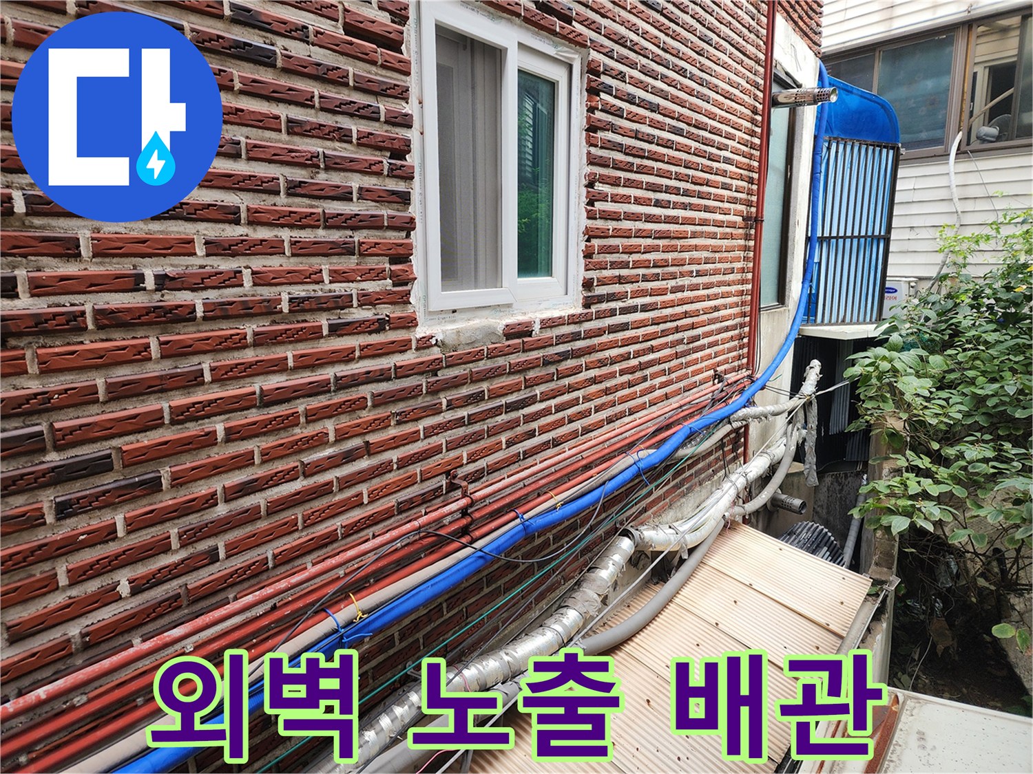 붉은 벽돌 외벽에 설치된 은색 및 파층 배관-동파 위험 구간 점검