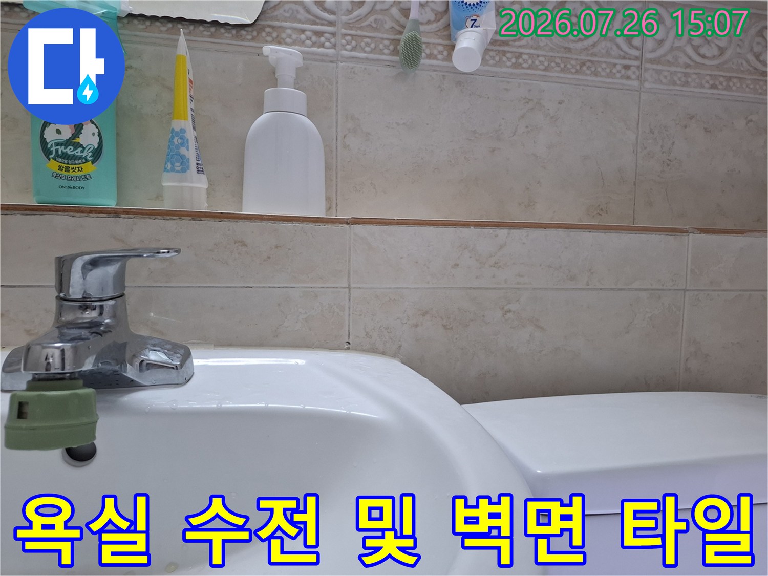 금속 재질의 세면대 수도꼭지와 베이지색 격자무늬 욕실 타일-선반 위 세정제들