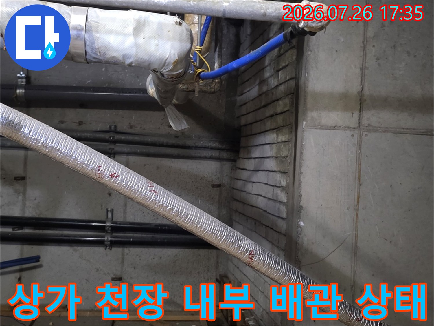 천장 슬래브 아래로 복잡하게 얽혀 있는 금속 배관과 파란색 호스-누수 점검 현장