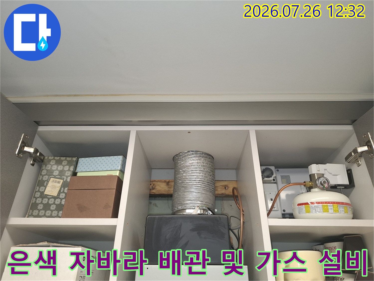 수납장 칸에 설치된 은색 주름관-우측에는 하얀색 가스통과 보일러 부품이 위치함