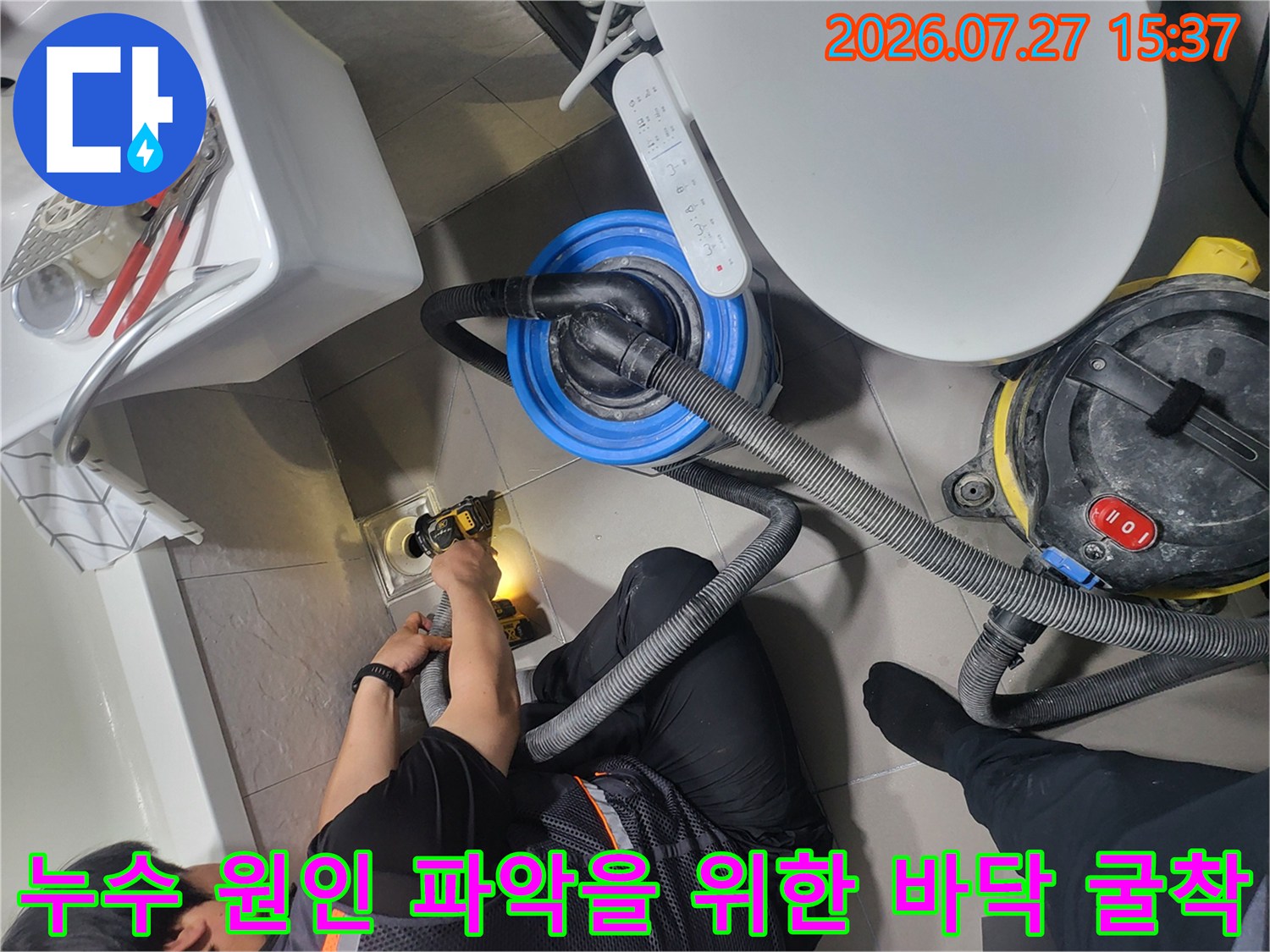 작업자가 전동 드릴을 사용하여 욕실 배수구 주변의 타일과 시멘트를 제거하는 정밀 작업 장면