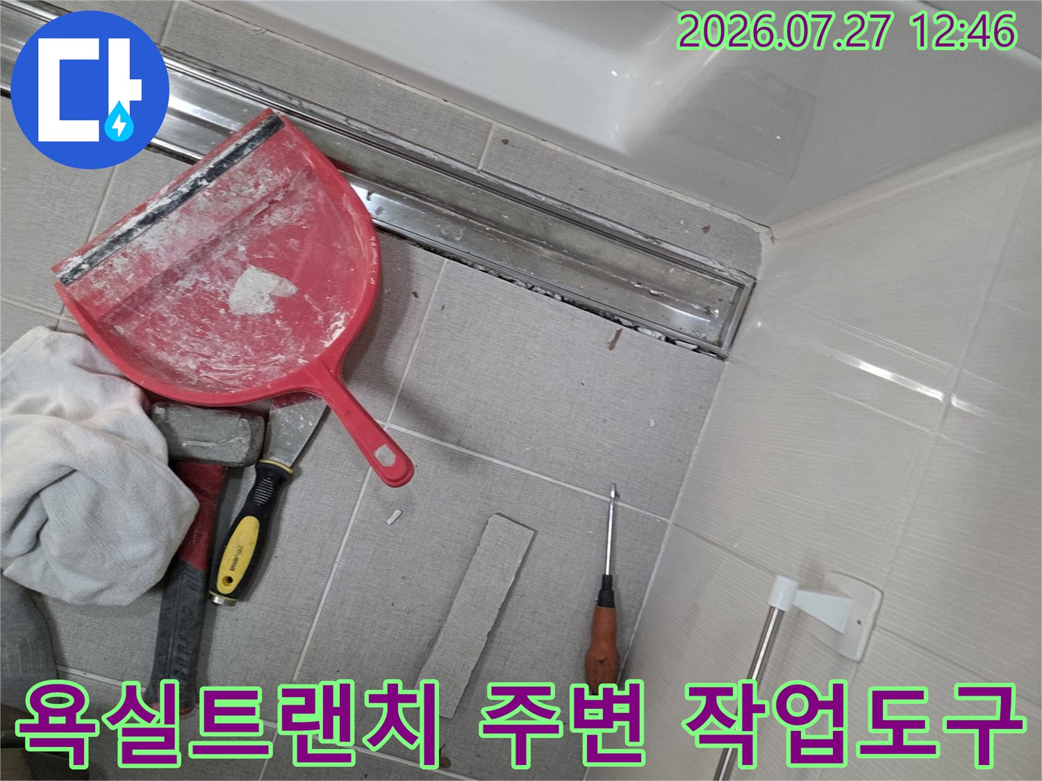 욕실 바닥의 금속제 트랜치 배수구와 그 주변에 놓인 빨간색 헤라-드라이버-수건 등의 작업 도구들