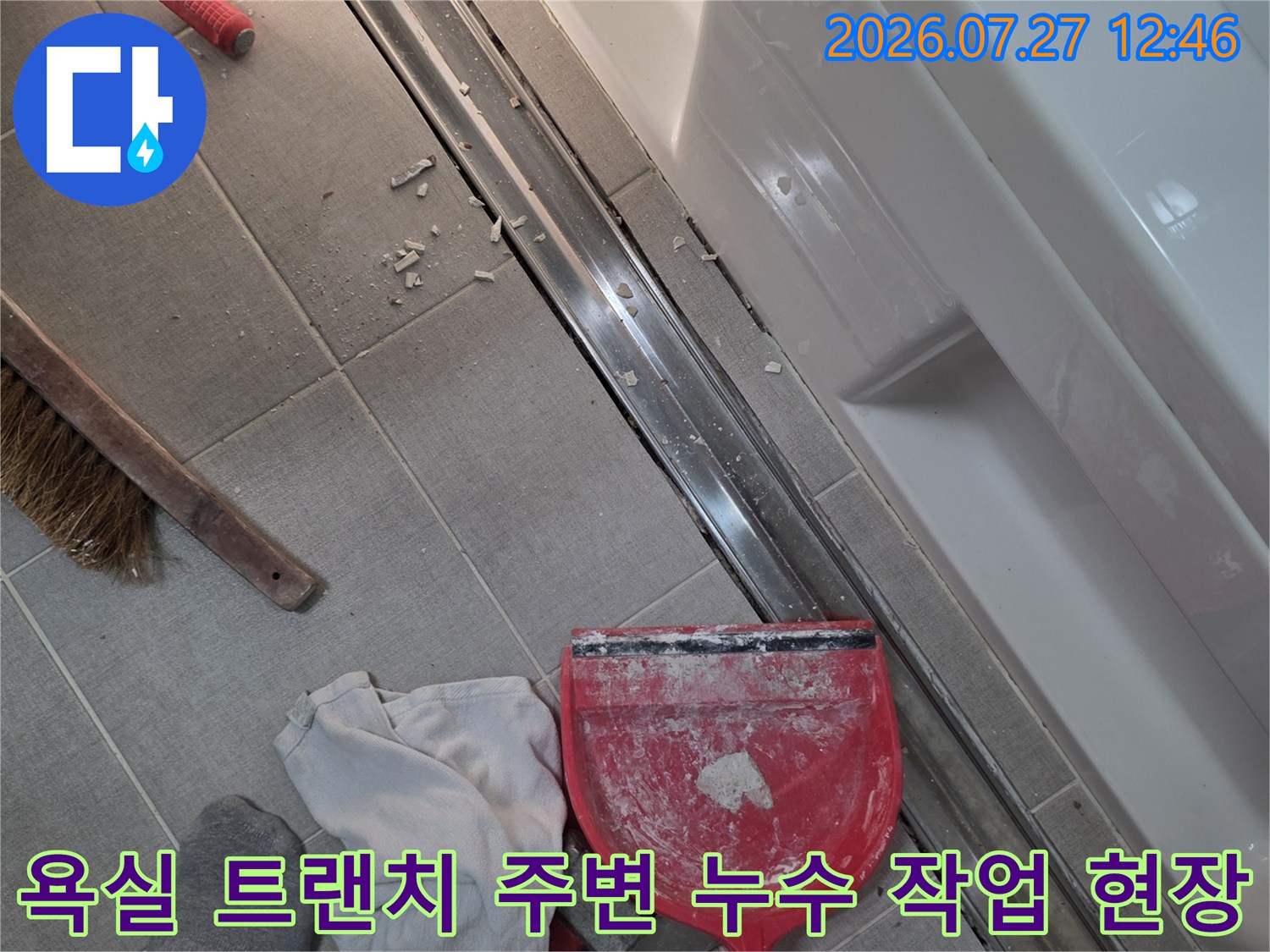 욕실-바닥의-긴-트랜치-배수구-주변에-빨간색-쓰레받기와-청소도구가-놓여있는-모습