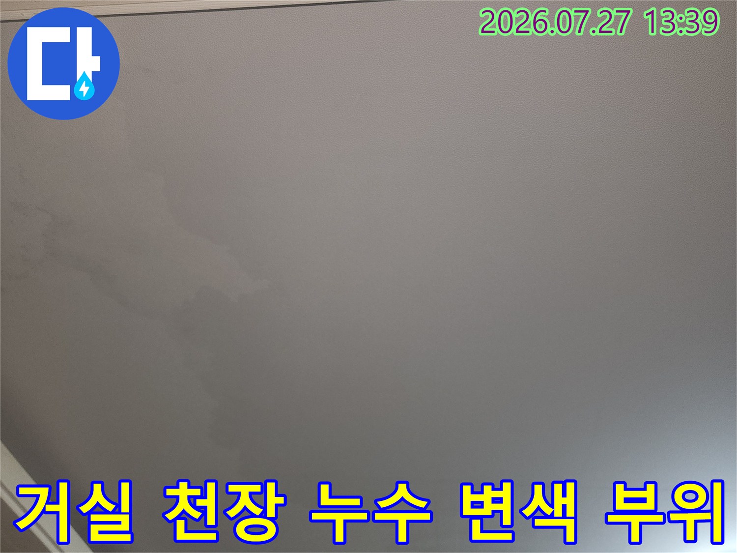 거실 천장의 흰색 벽지가 누수로 인해 누렇게 변색되고 얼룩진 모습