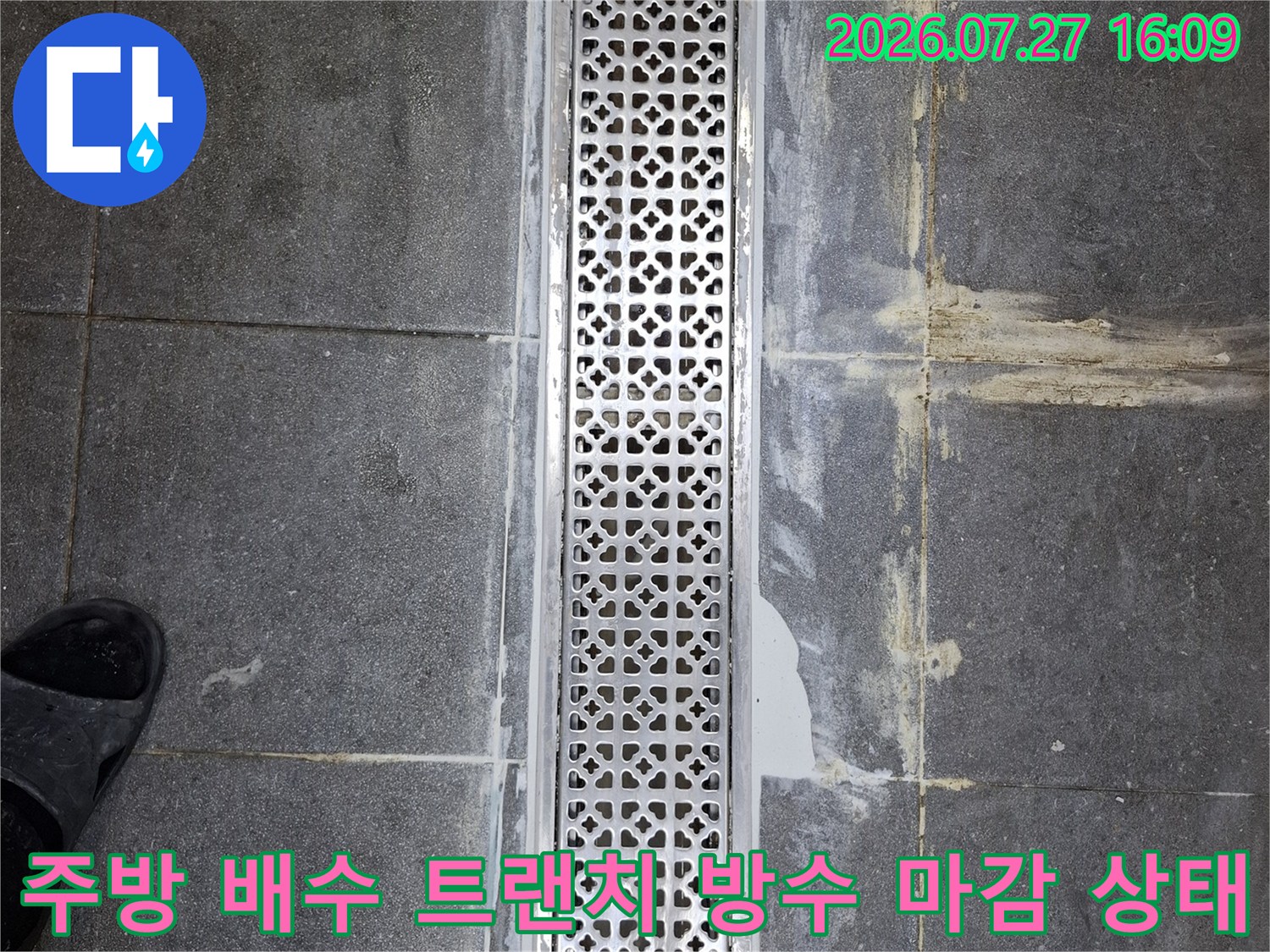 회색 타일 바닥에 설치된 금속제 배수 트랜치-주변 마감재의 오염과 틈새가 보이는 모습