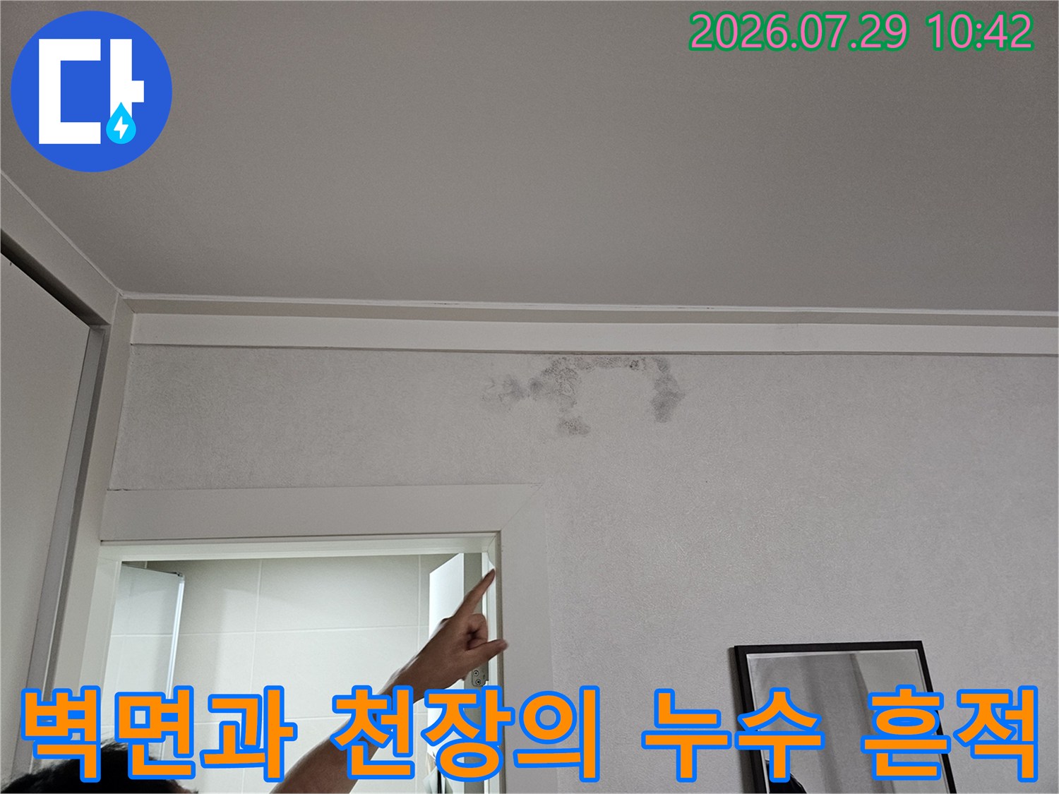 천장 모서리 부근에 발생한 습기 얼룩을 손으로 가리키며 설명하는 모습