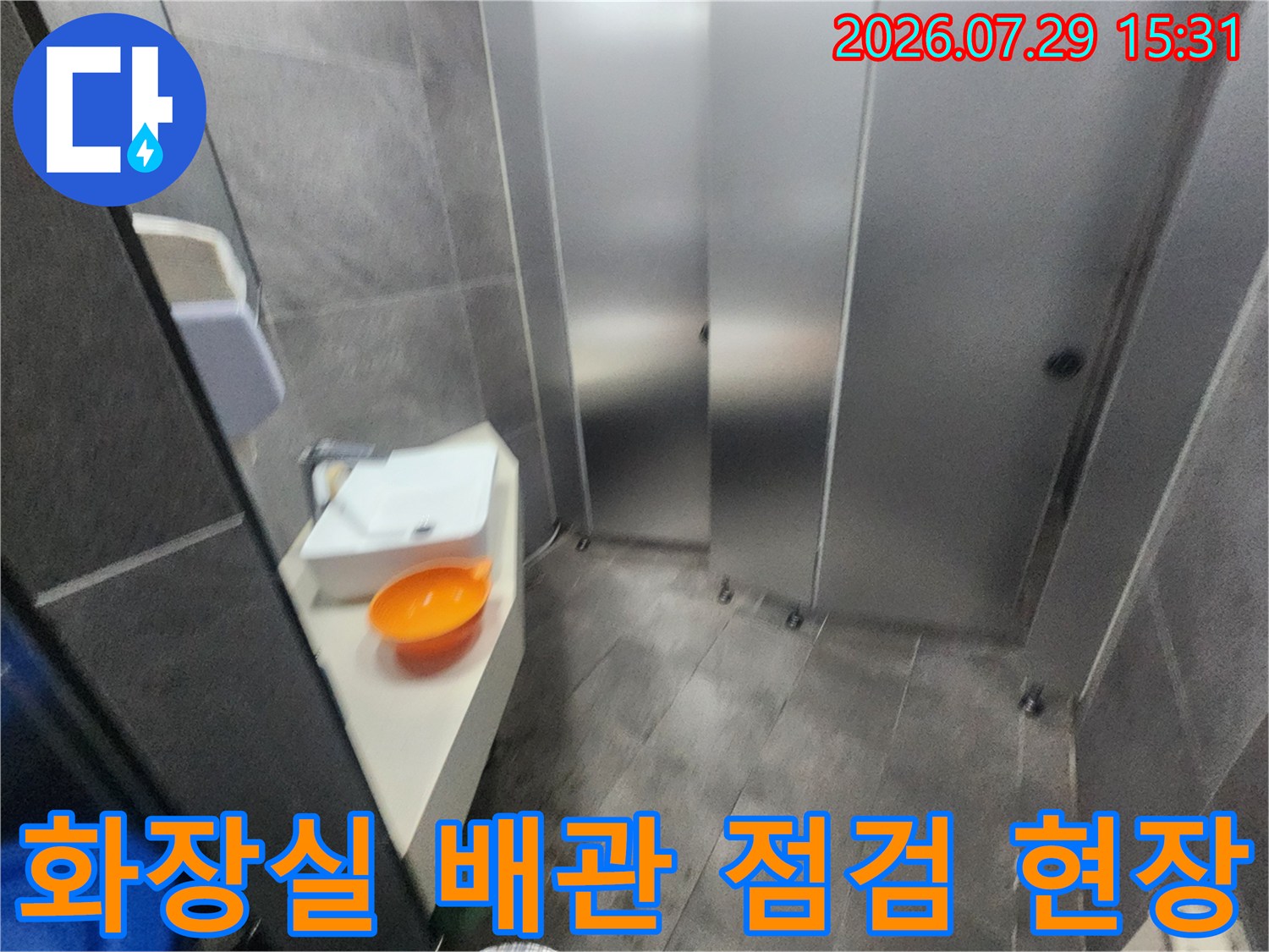 금속 재질의 화장실 문과 바닥 타일로 구성된 내부 공간에서 진행되는 누수 점검 작업
