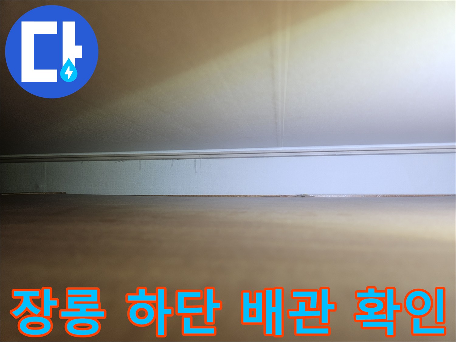 장롱 밑 좁은 공간 내 배관 연결 부위의 상태를 점검하는 장면입니다.
