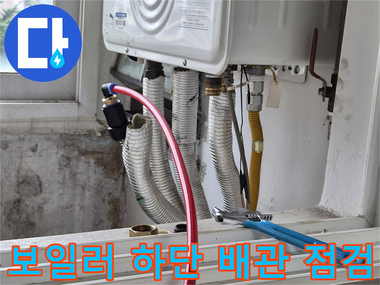 붉은색 호스가 연결된 보일러 하부 배관과 공구