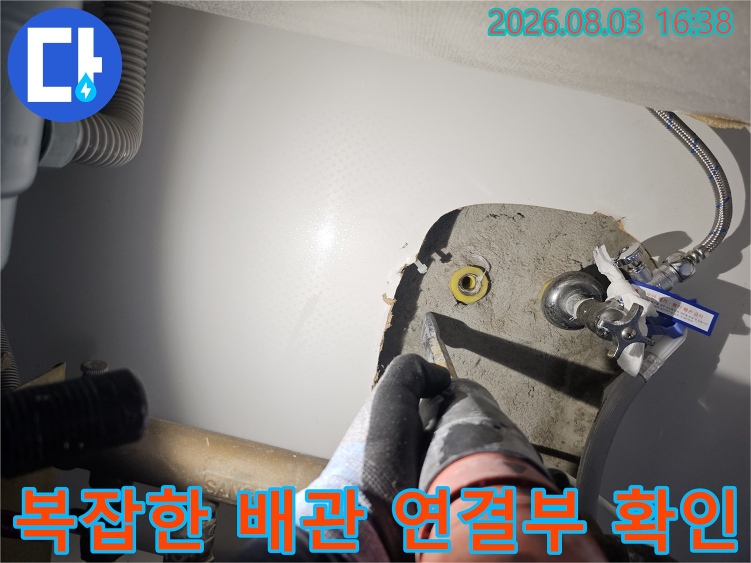 작업자가 싱크대 하단부의 노란색 및 회색 배관 연결 부위를 손으로 만지며 점검하는 모습