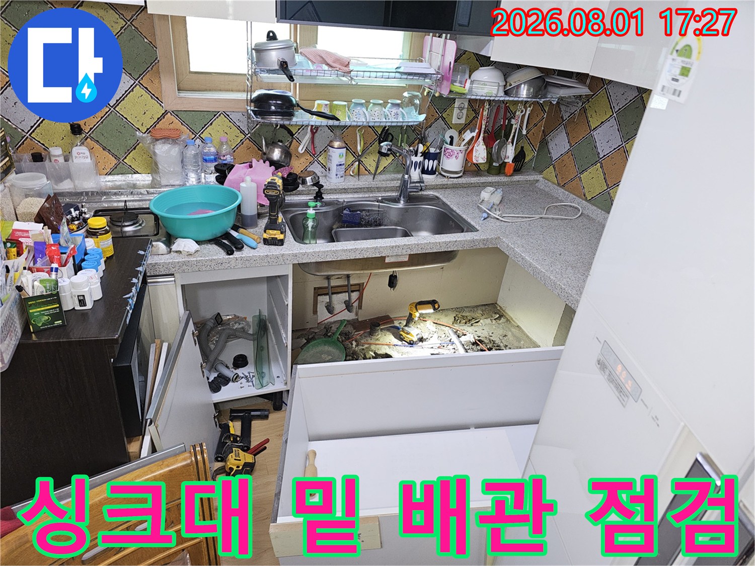 작업자가 싱크대 하부 공간에서 노출된 수도 배관을 정밀하게 점검하는 모습