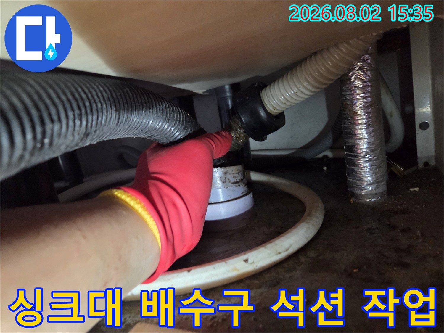 빨간 장갑을 낀 작업자가 싱크대 하단 배수관에 석션 호스를 연결하여 이물질을 제거하는 모습